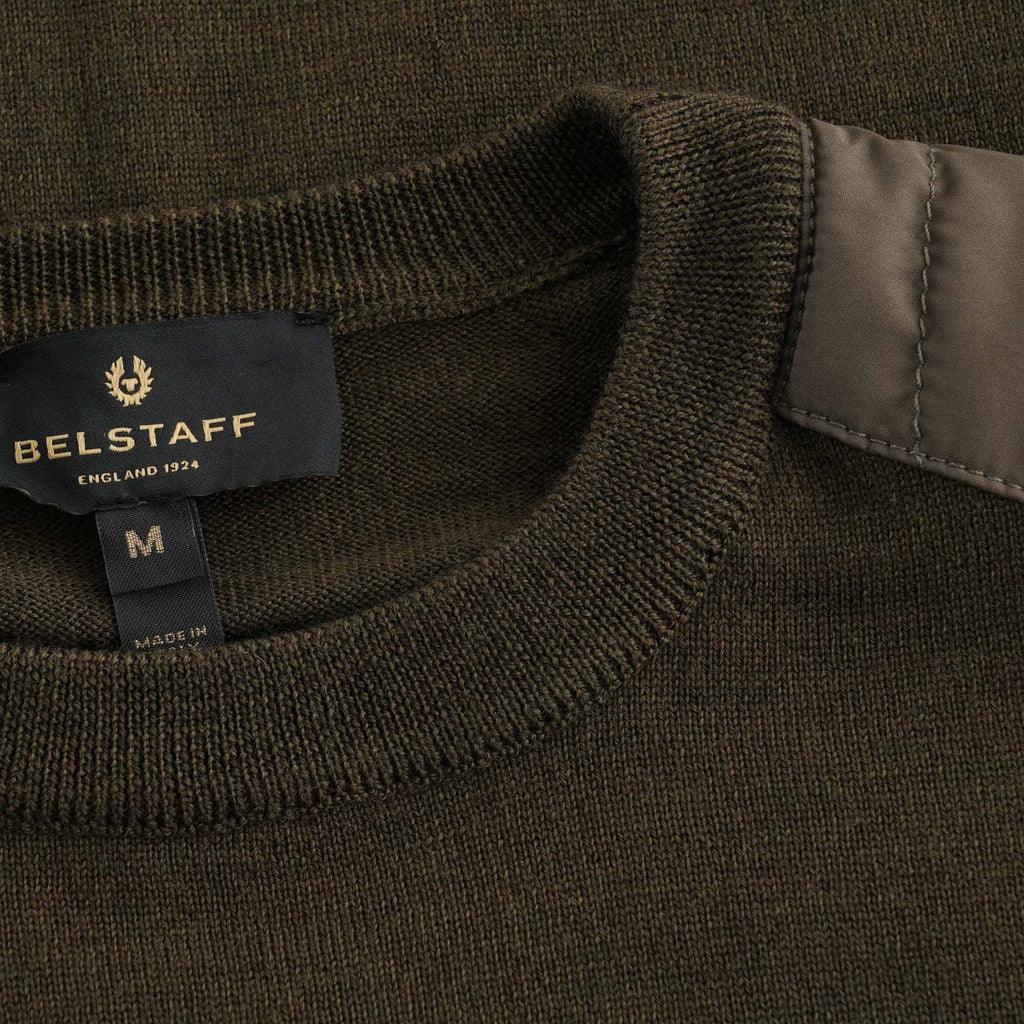 Close-up of the Belstaff brand label and neck of the dark green men's jumper.
