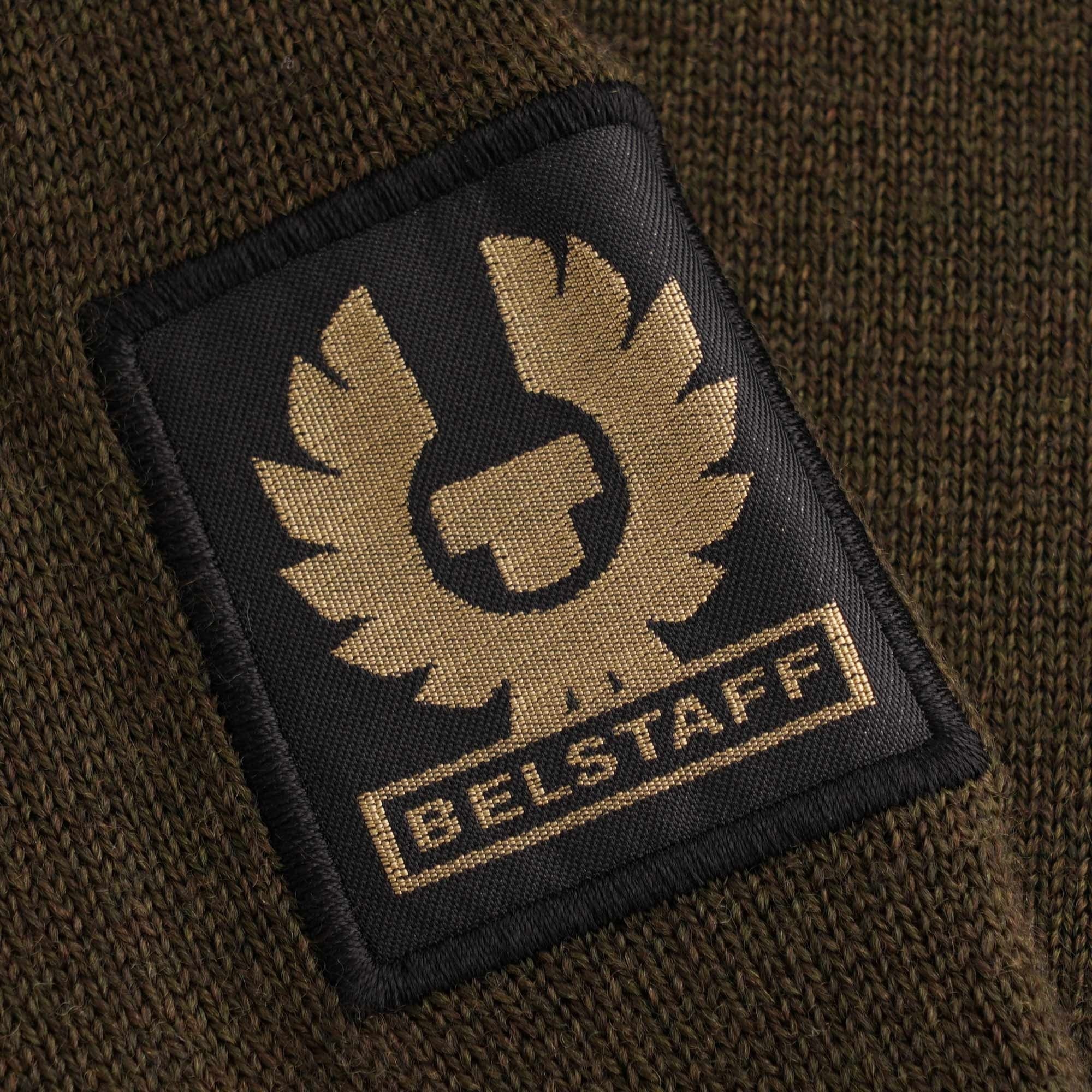 Close-up of the Belstaff Phoenix logo patch on the arm of the dark green jumper.