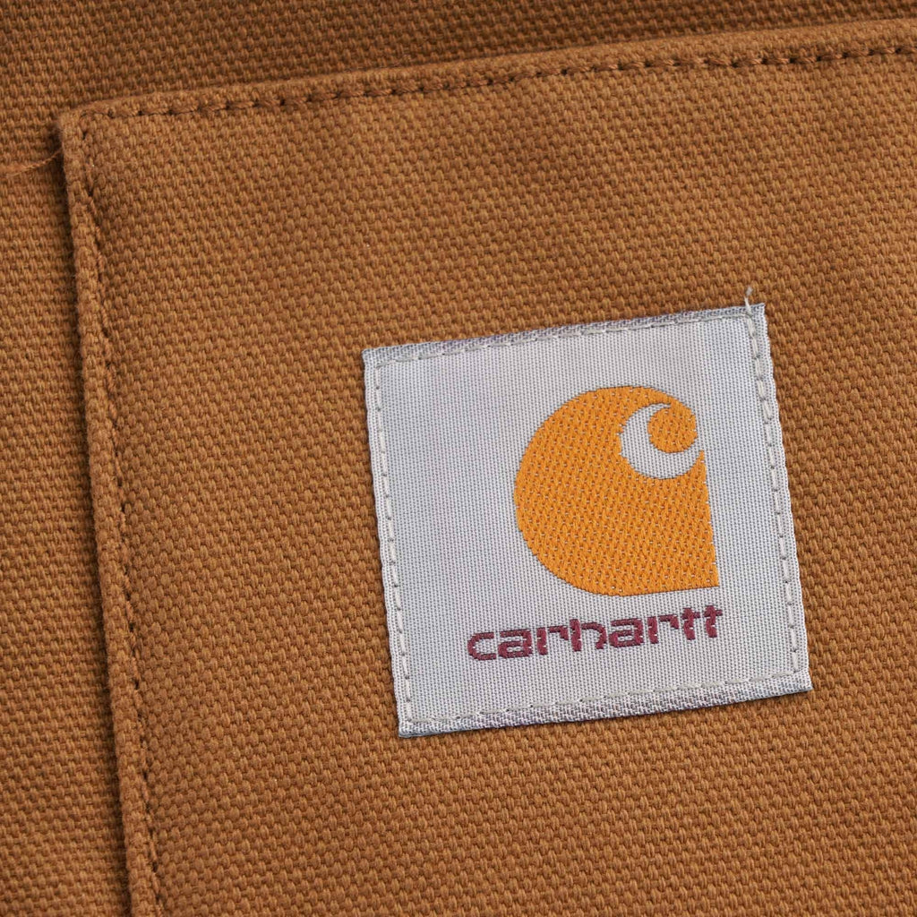 Close-up of the iconic Carhartt 'C' logo patch on the front pocket of the brown vest.