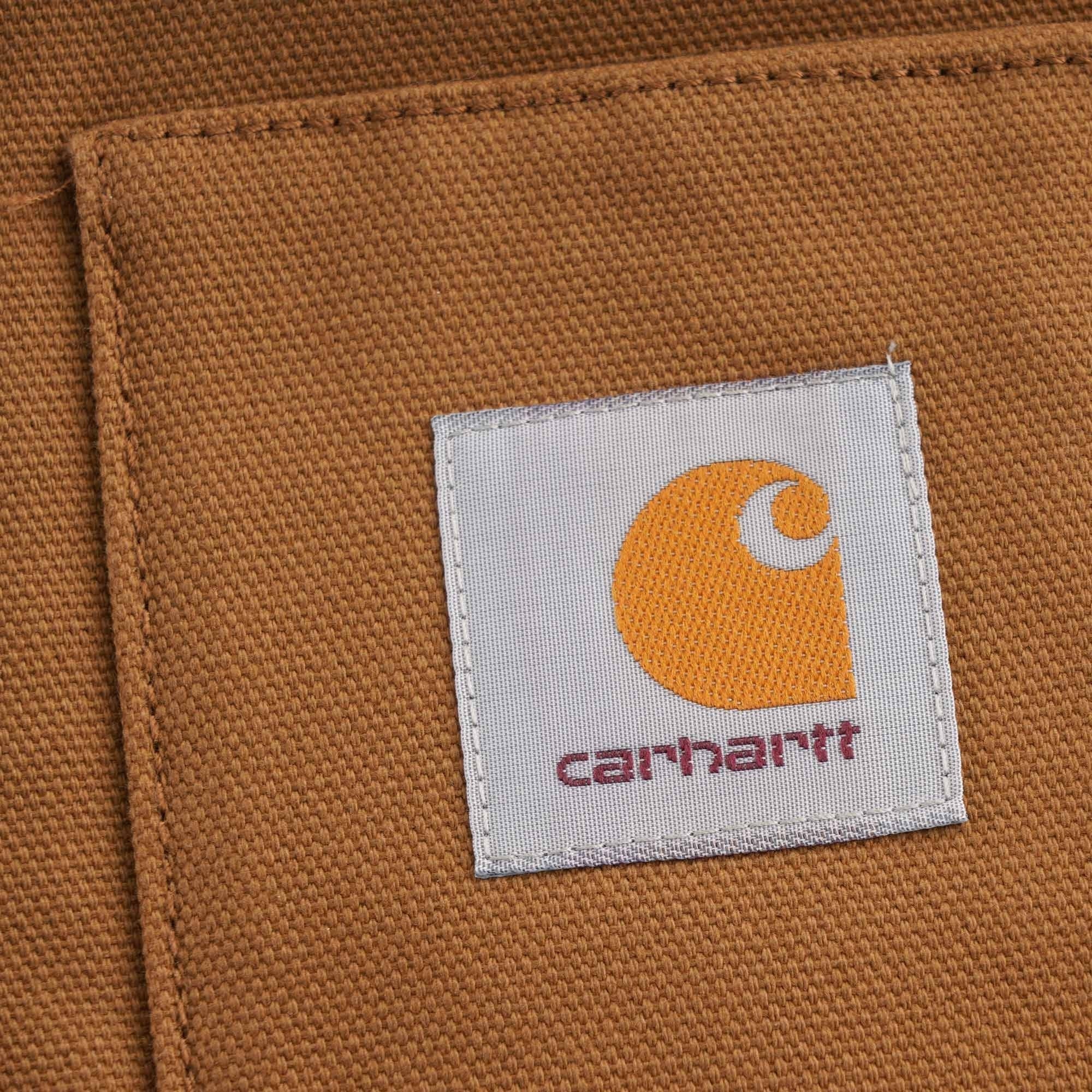 Close-up of the iconic Carhartt 'C' logo patch on the front pocket of the brown vest.