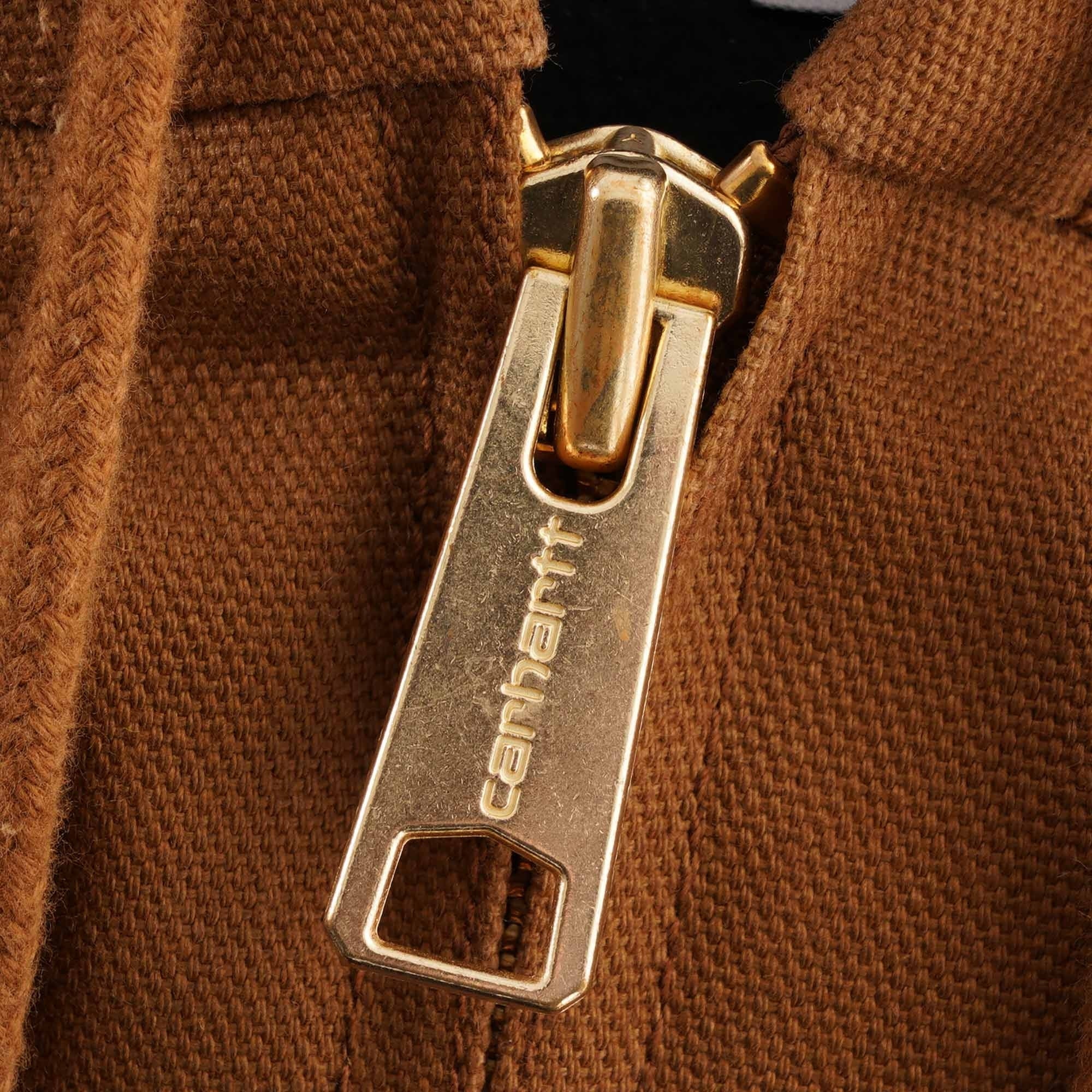 Close-up of a gold Carhartt branded zip on a brown jacket.