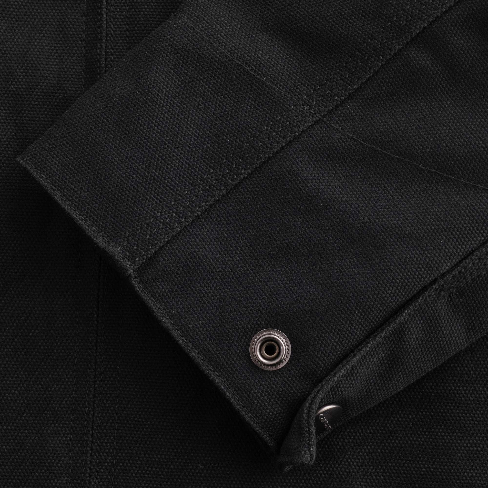 A close-up of the cuff of a black jacket with a snap button detail.