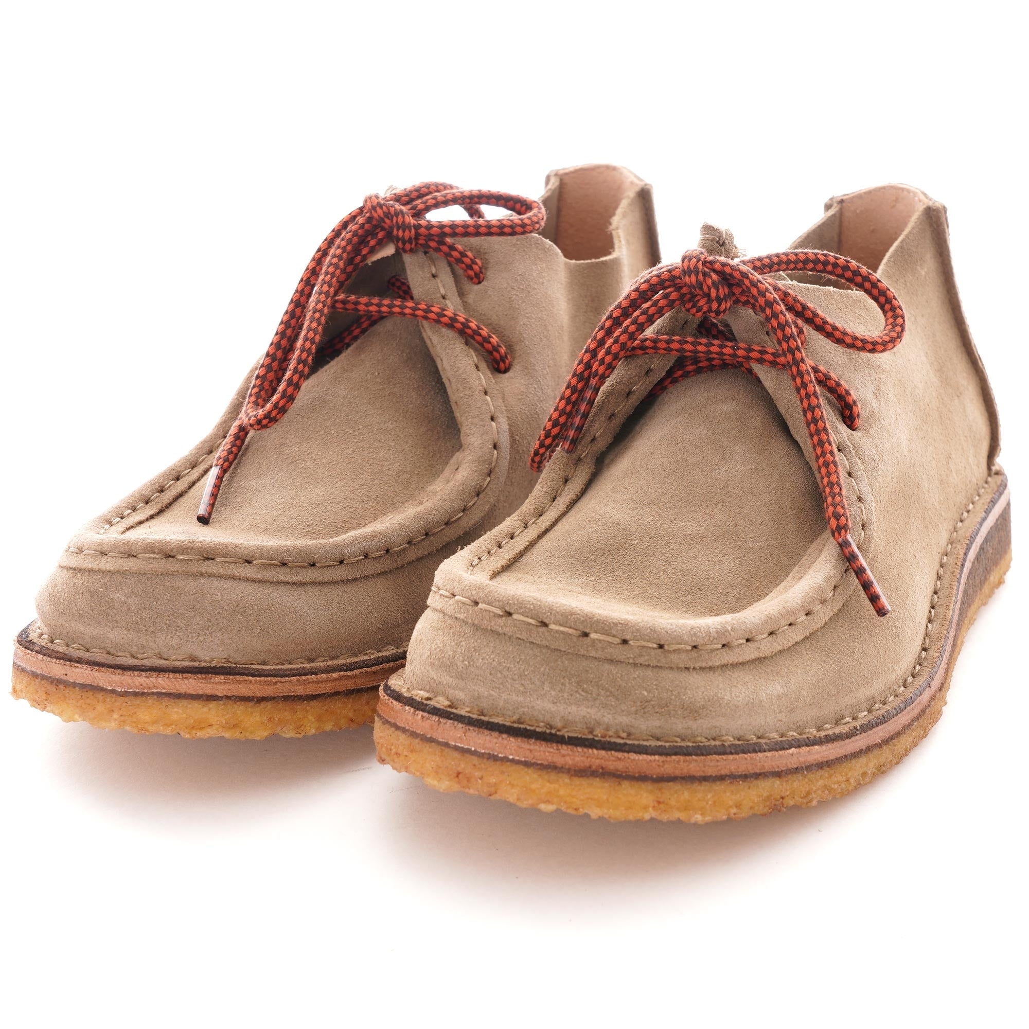 A pair of taupe suede shoes with red and black laces, viewed from the front.