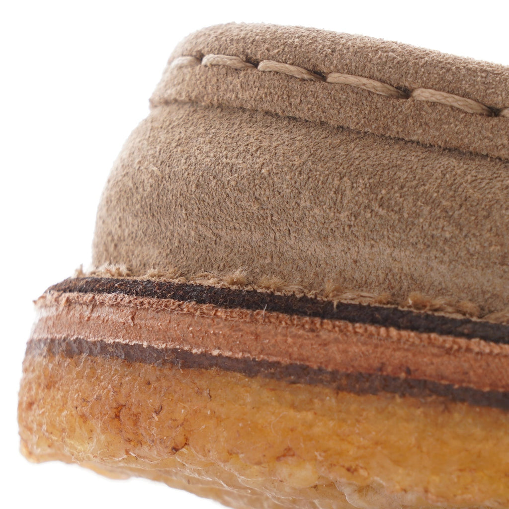 A close-up of the sole and stitching on a taupe suede shoe.