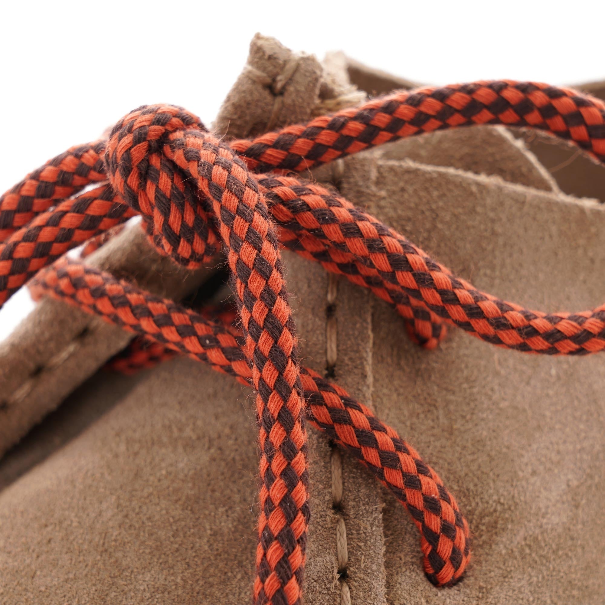 A close-up of the red and black patterned shoelaces tied on a taupe suede shoe.