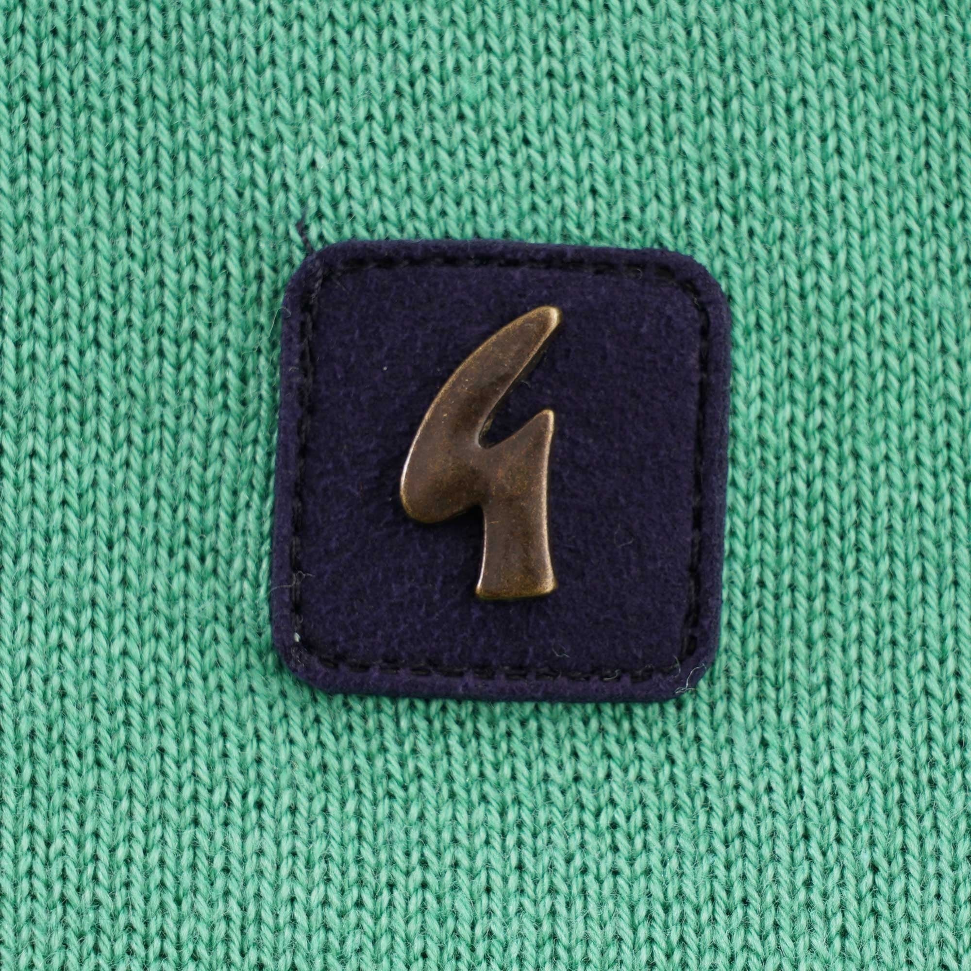 A close-up of the brand logo on the green knitted polo shirt.