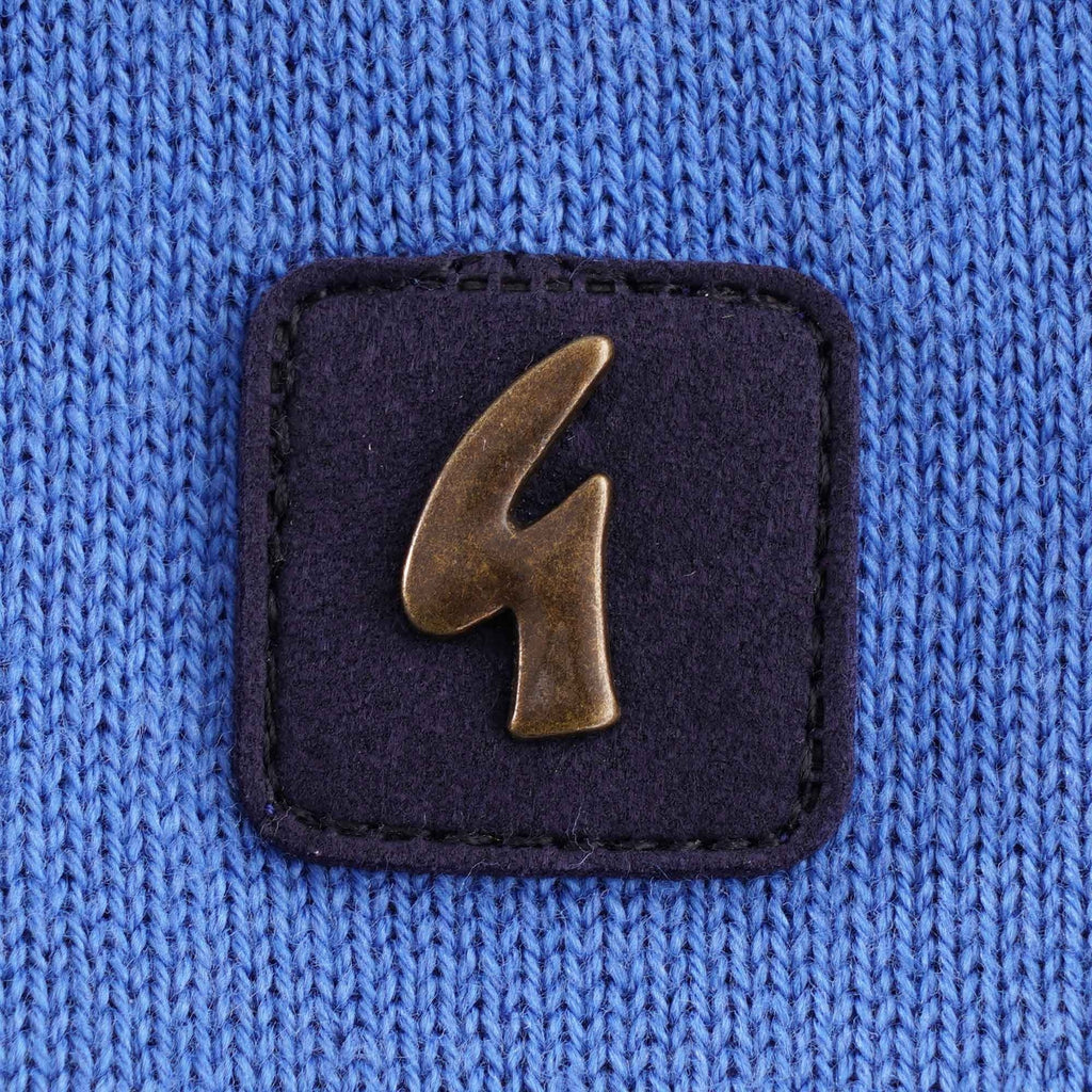 Close-up of a square dark blue patch with a bronze 'G' logo on the polo shirt.