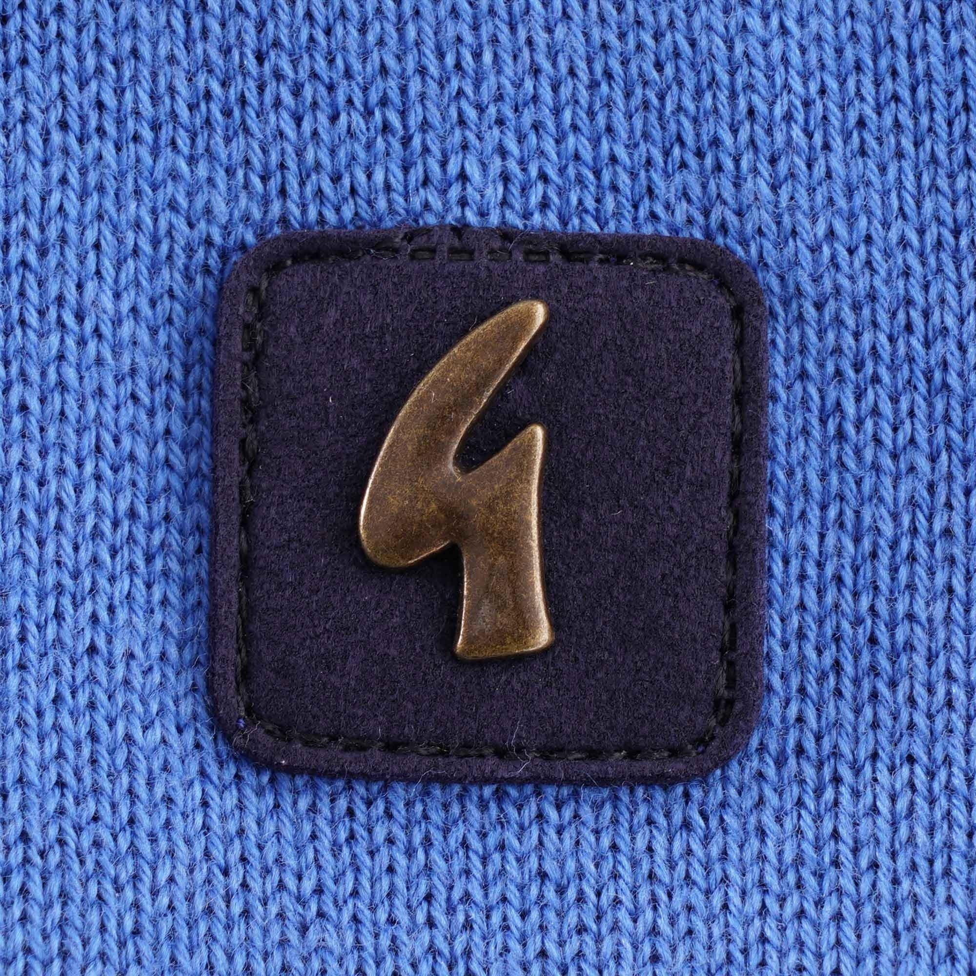 Close-up of a square dark blue patch with a bronze 'G' logo on the polo shirt.