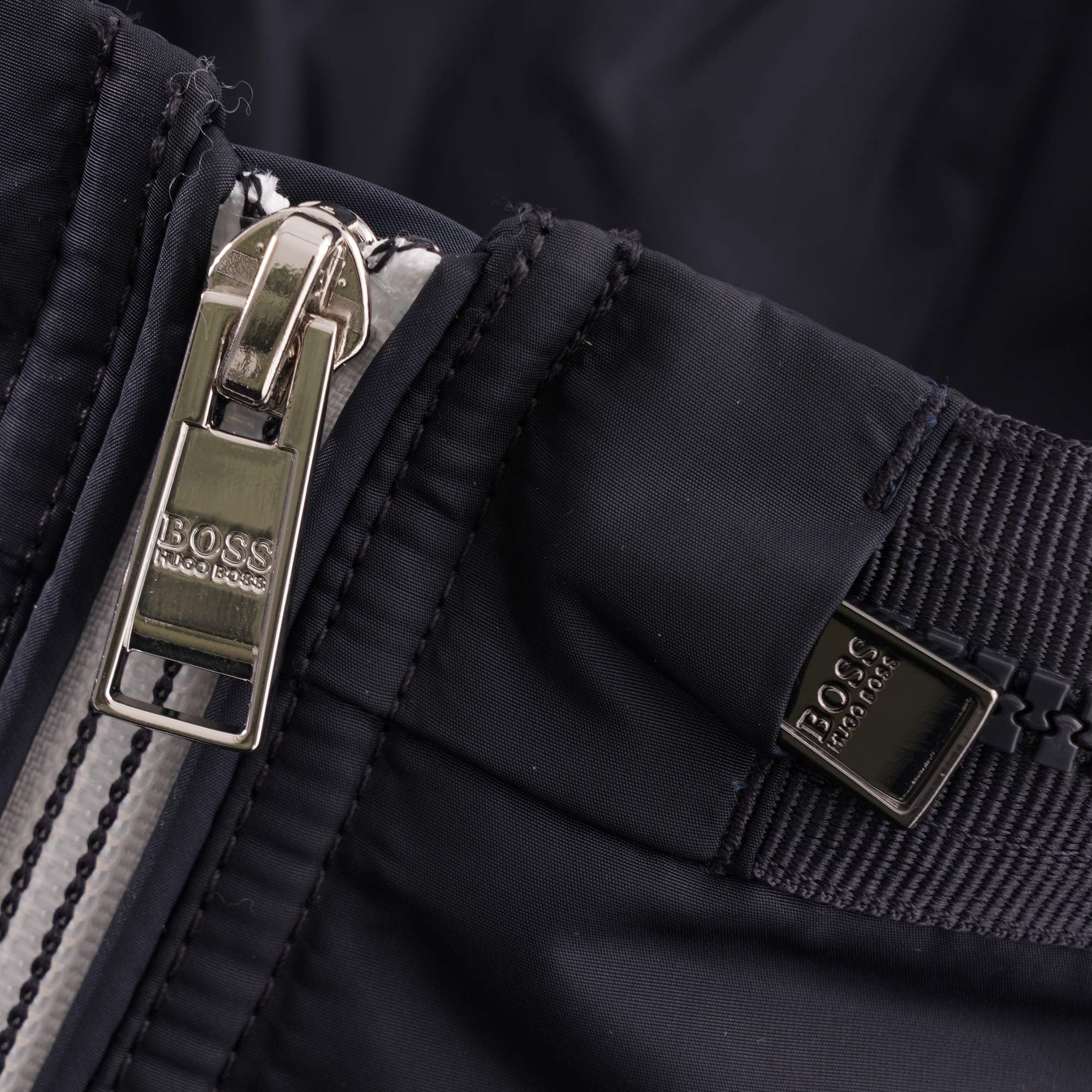 Detail of the jacket's main zip puller and a branded metallic tag.