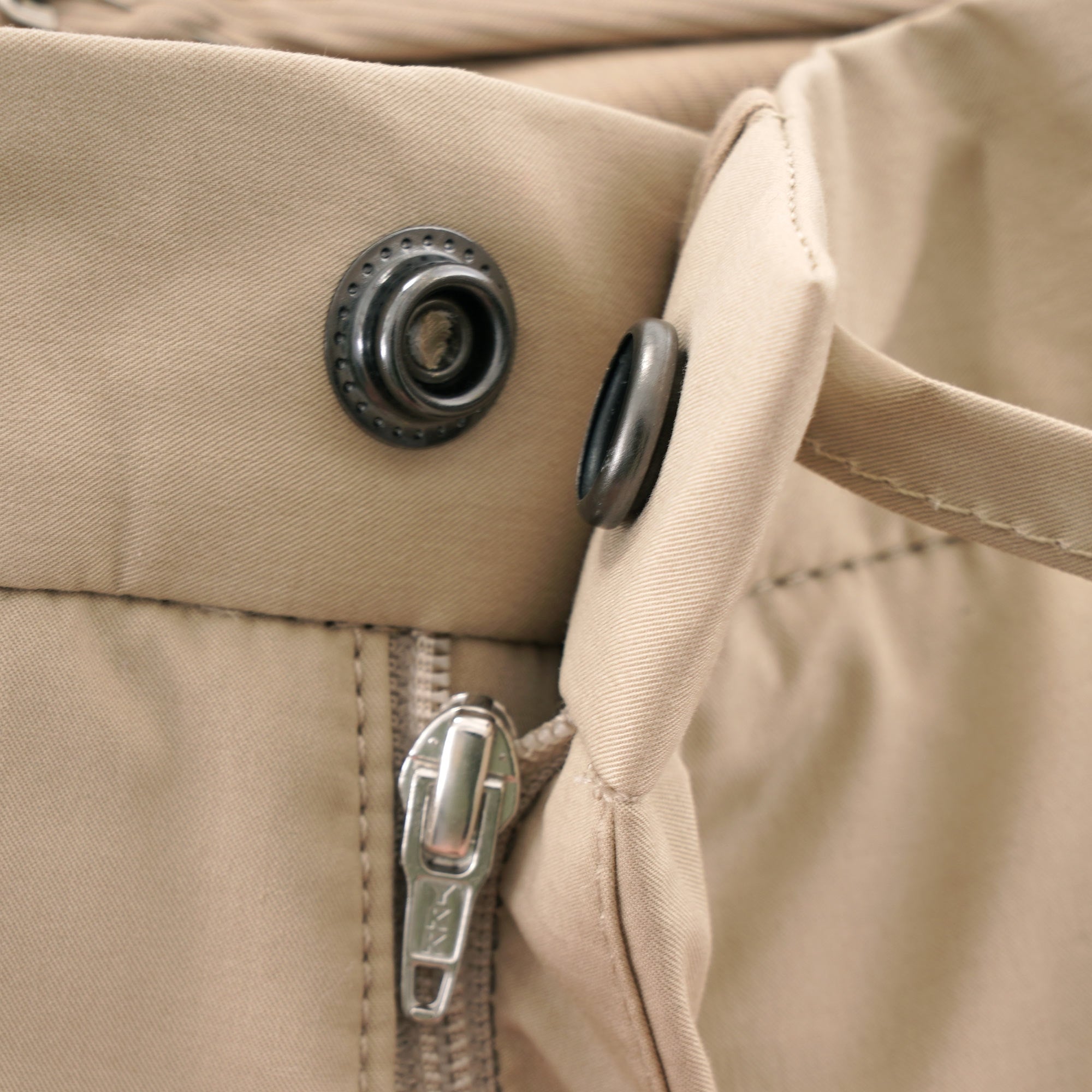 Close-up of the zipper and snap button closure on beige trousers.