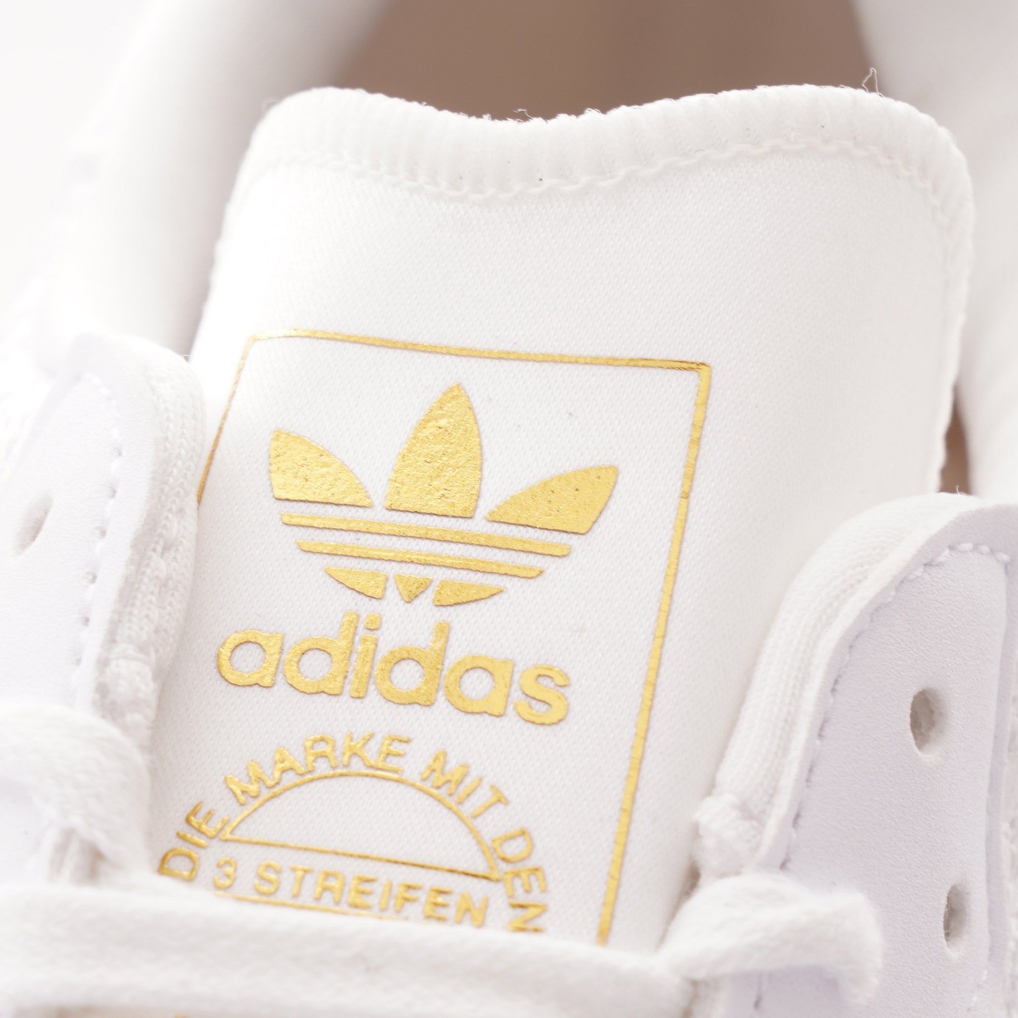 Close-up of the gold Adidas logo on the tongue of a white Sambarose trainer.
