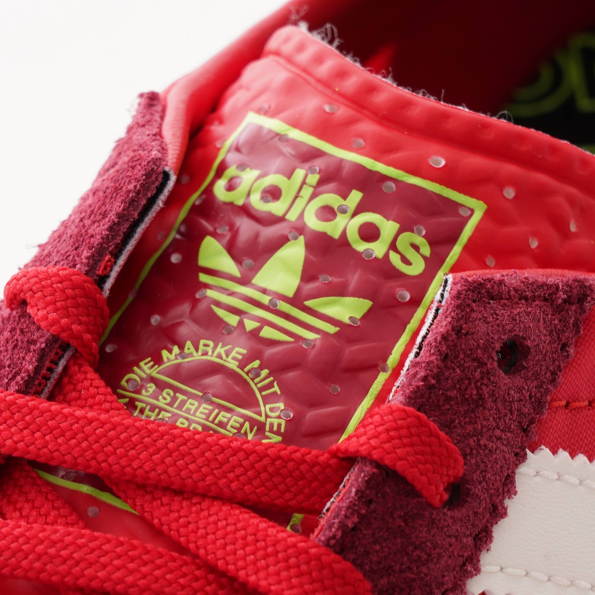 A close-up shot of the red tongue of an adidas trainer with a yellow logo.