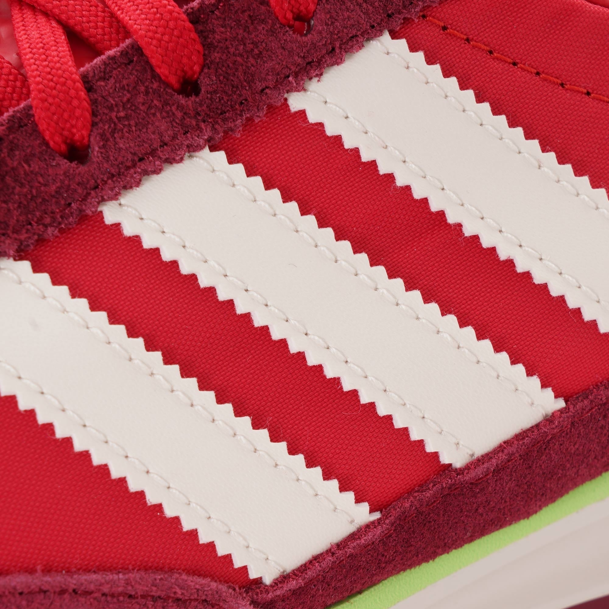 A close-up shot of the white stripes on the side of a red adidas SL 72 RS trainer.