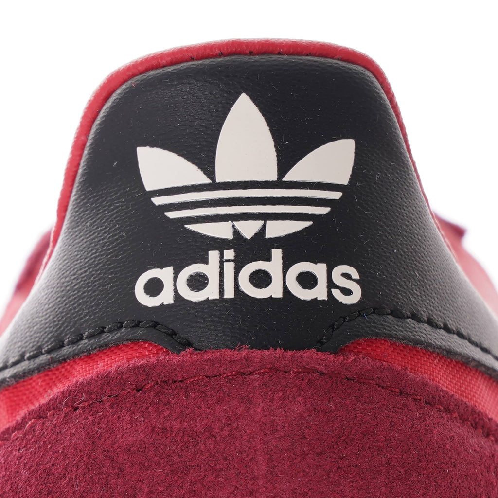 A close-up shot of the black heel tab with the white adidas trefoil logo on a red trainer.