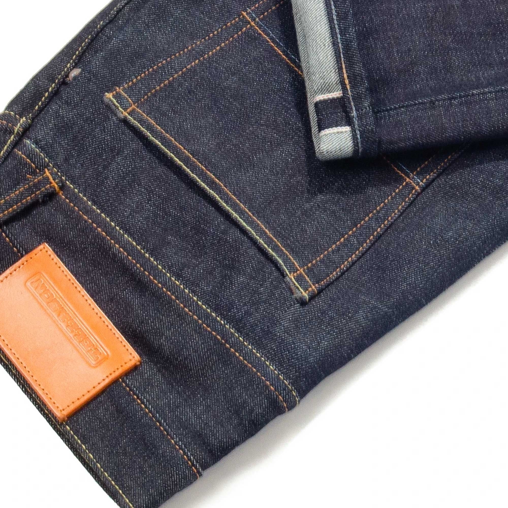 Detail of the back pocket, leather patch, and cuffed hem of dark wash selvedge denim jeans.