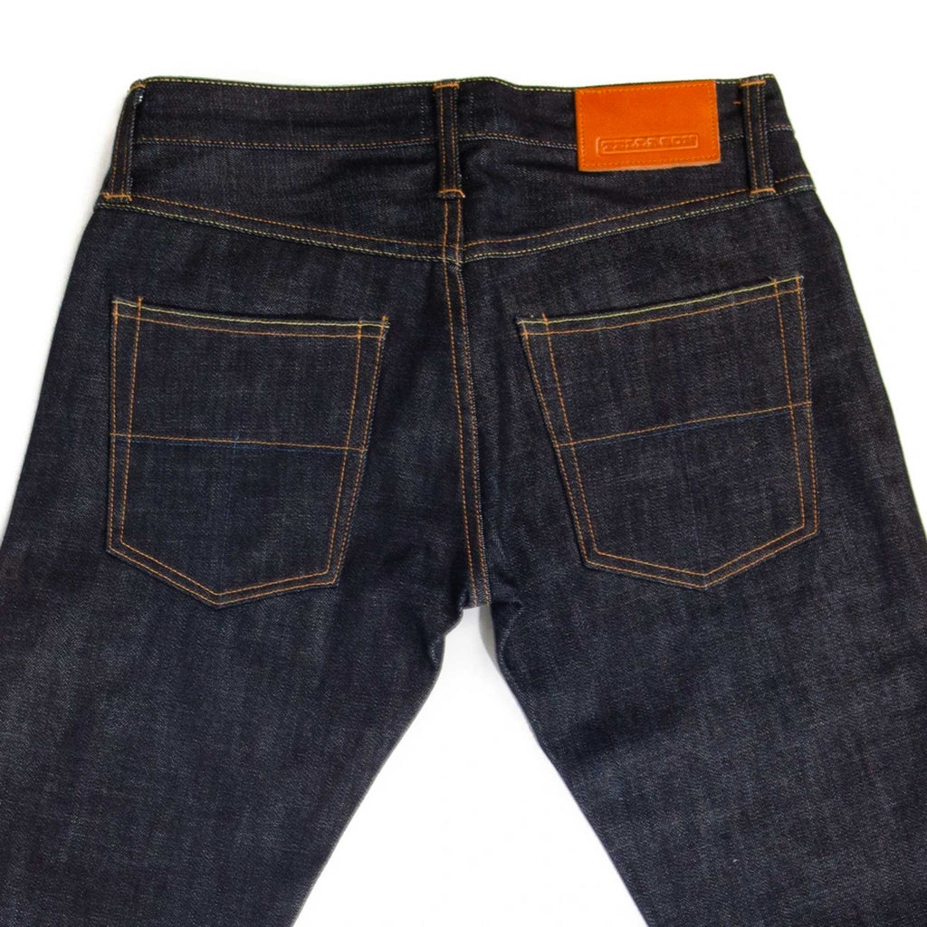 Rear view of dark blue denim jeans showing the pockets and a brown leather patch.