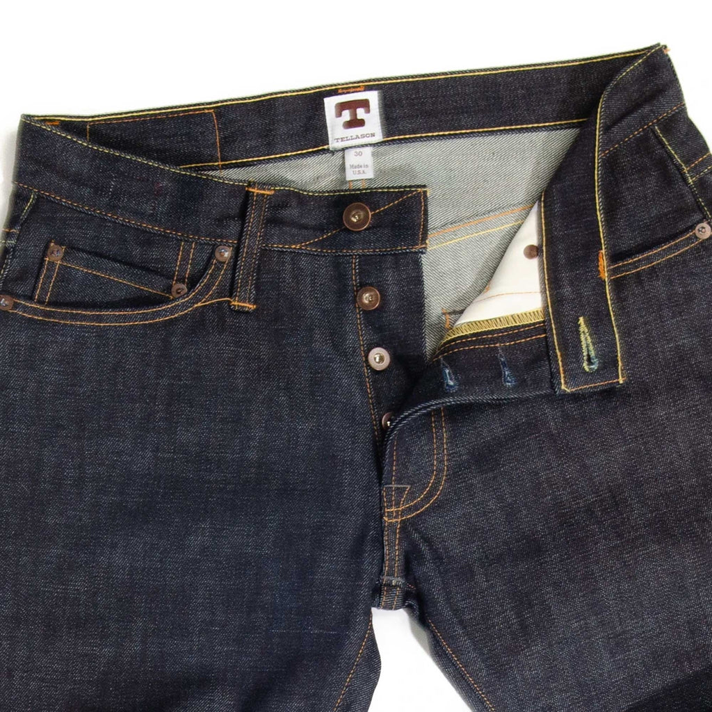 Close-up of the fly and waist of dark blue denim jeans with button details.