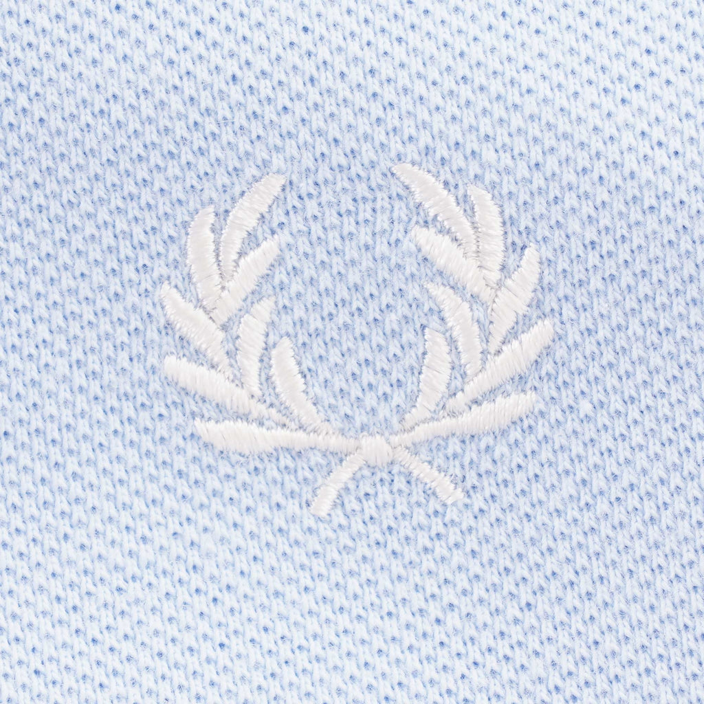 Close-up of the white embroidered Fred Perry laurel wreath logo on light blue fabric.