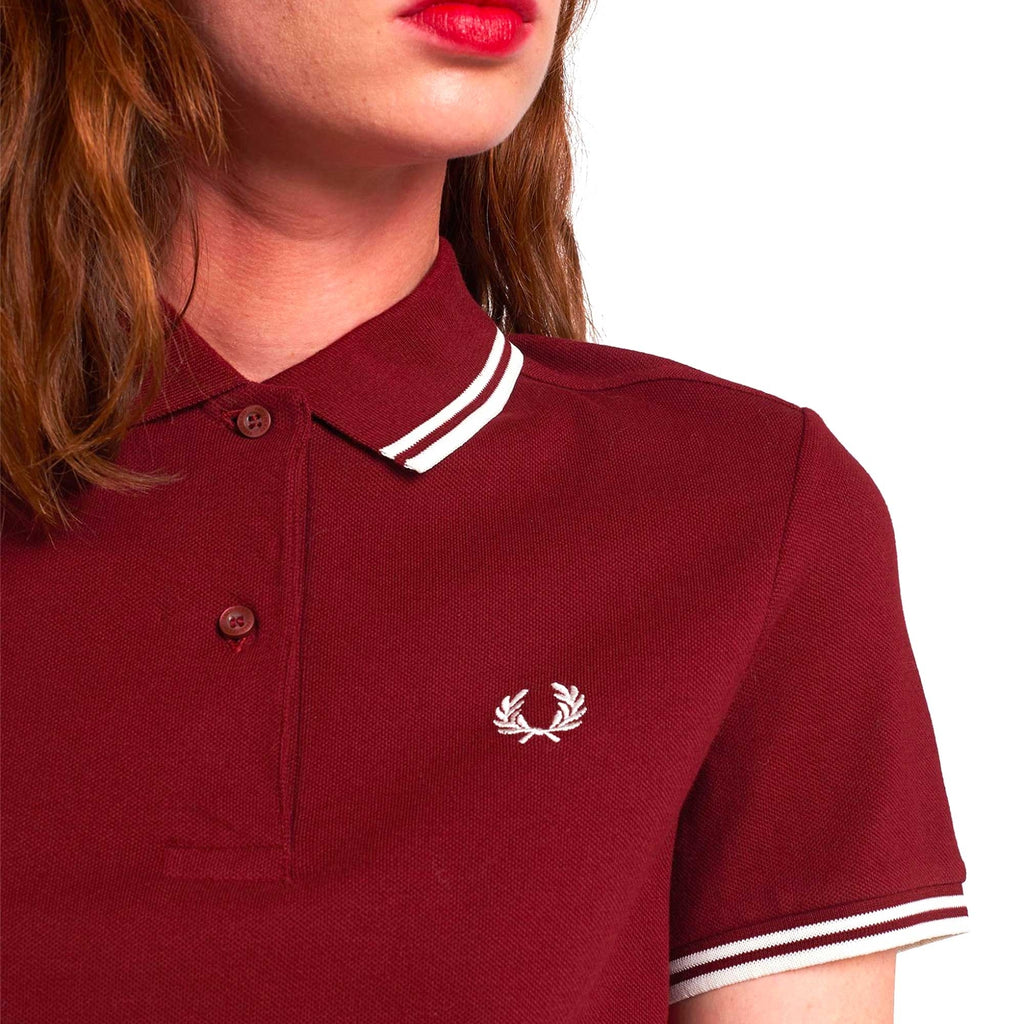 A close-up of a woman wearing a dark red Fred Perry polo shirt with white twin-tipping.