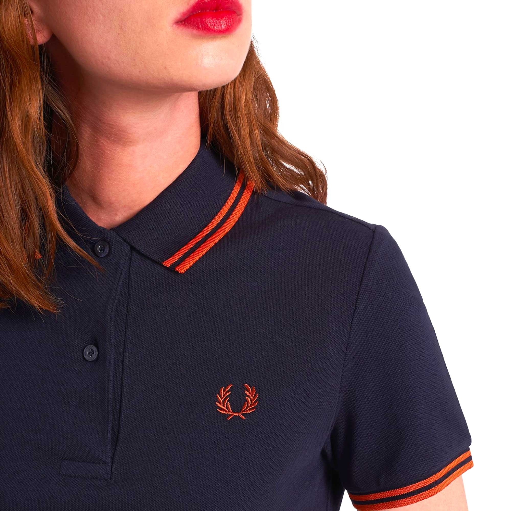A close-up of a person wearing a navy polo shirt with orange tipping, showing the collar detail.