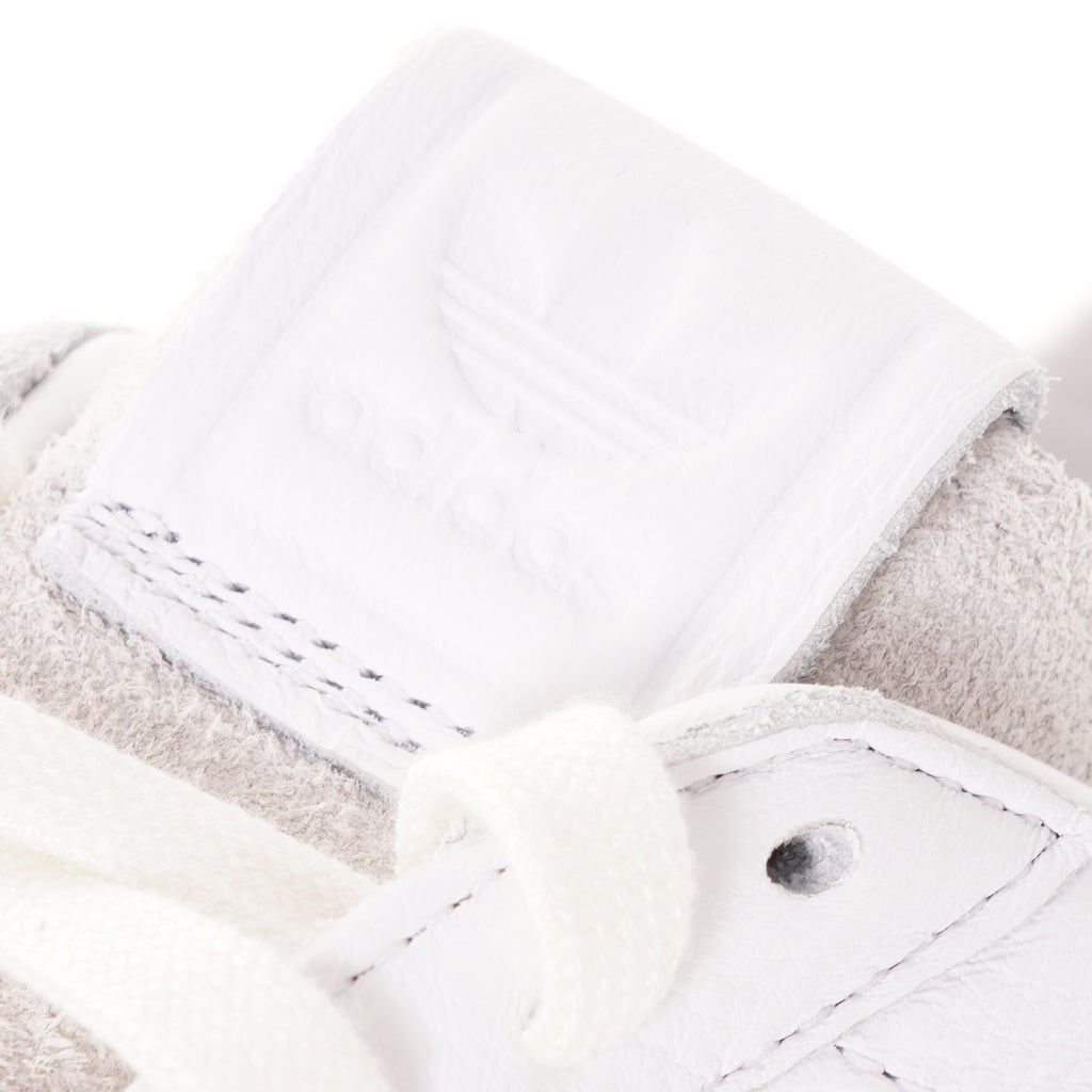 A close-up of the adidas logo embossed on the tongue of a white sneaker.