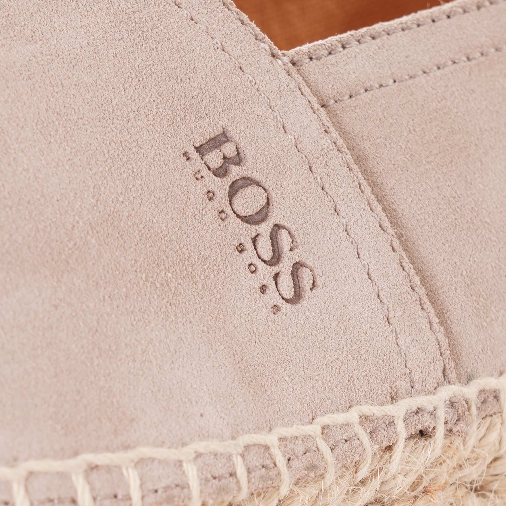 Close-up of the BOSS logo debossed on the light beige suede of an espadrille.