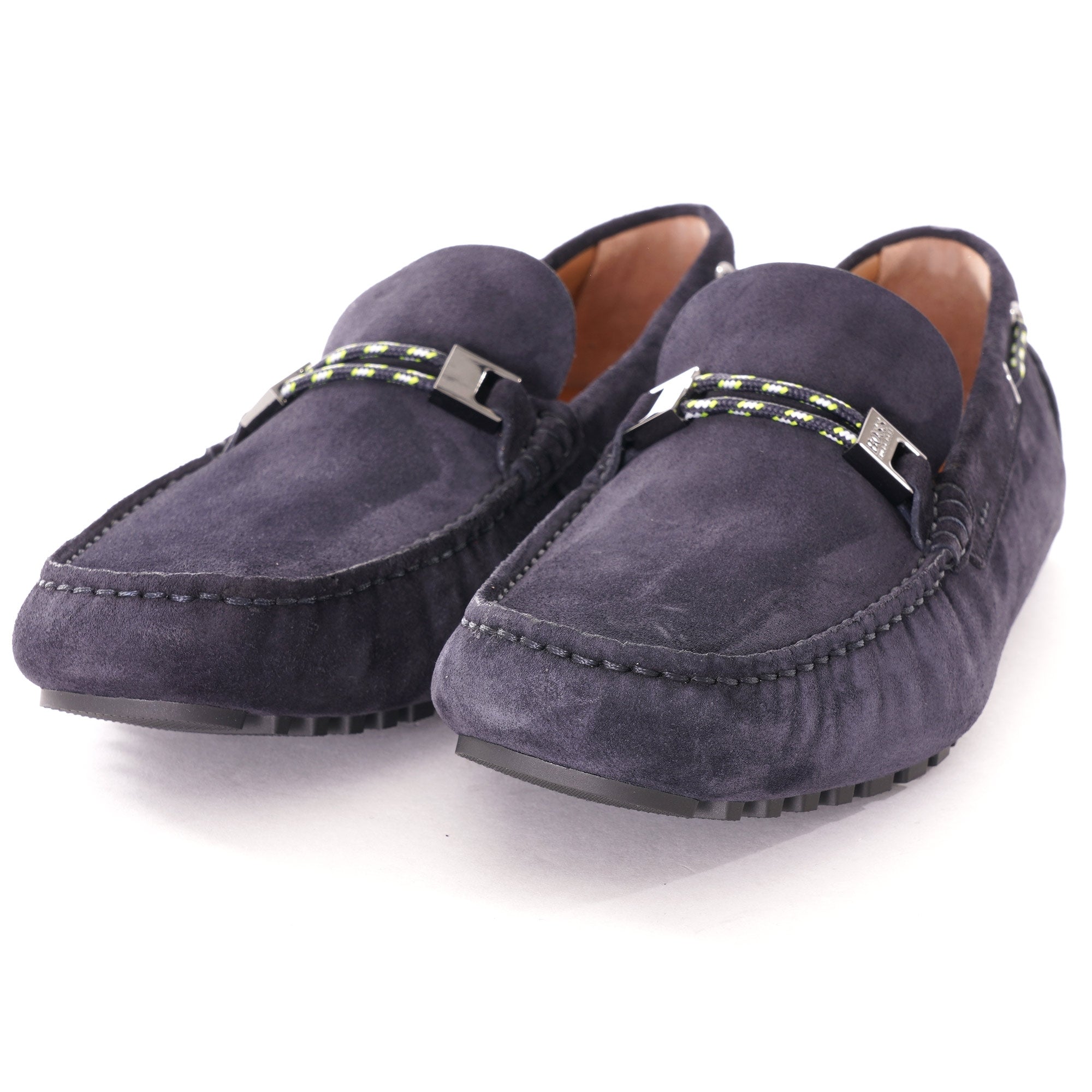 A pair of dark blue suede loafers with metallic buckles and striped detailing.