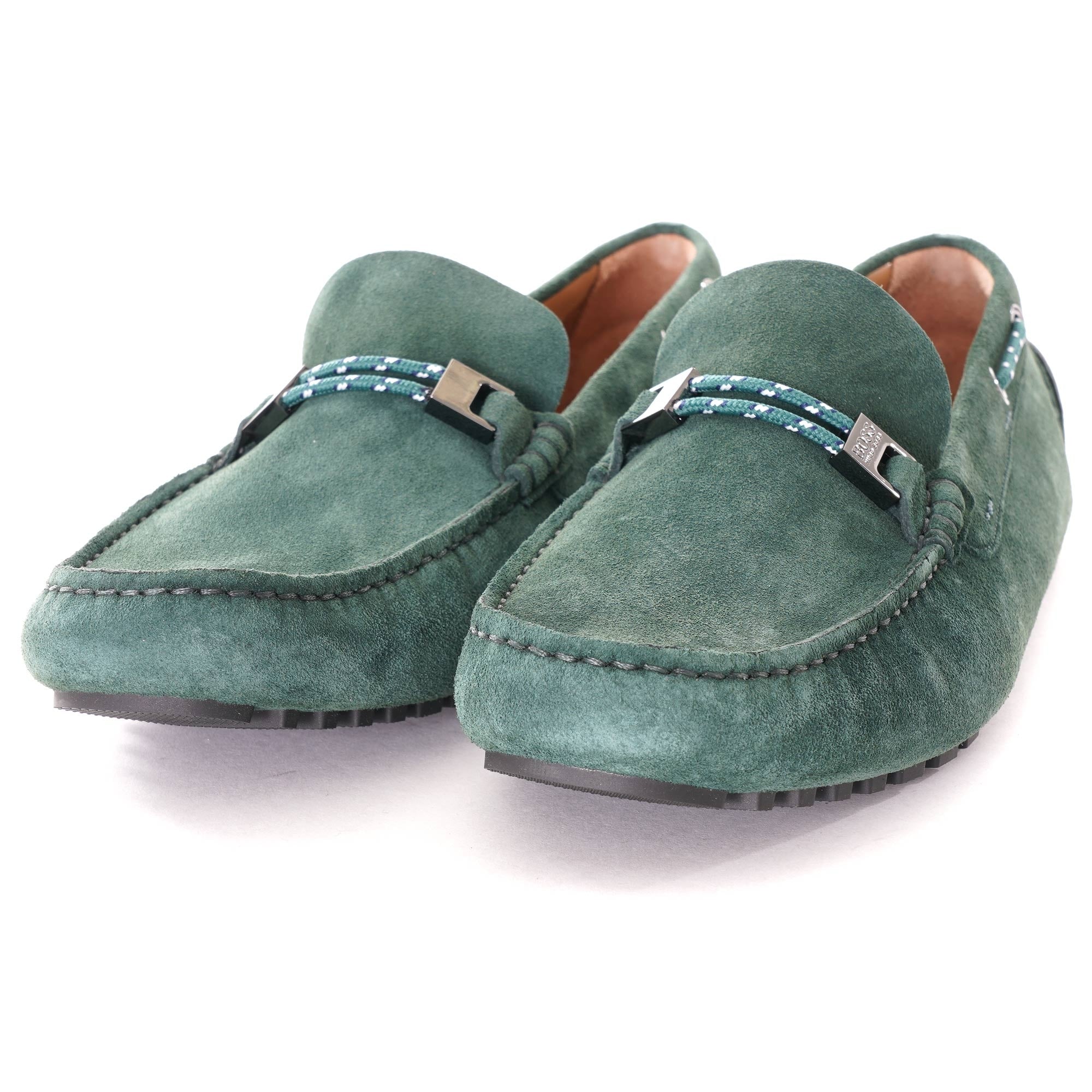 Pair of green suede loafers with grey buckles on a white background.