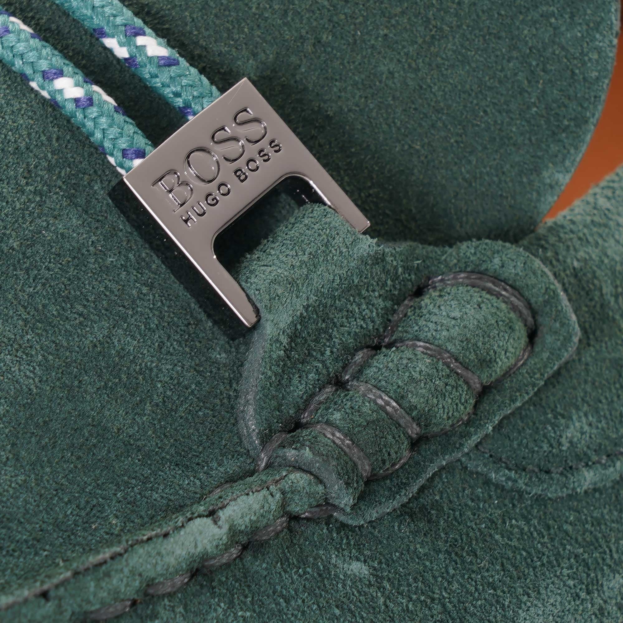 Close-up of the BOSS logo on the grey buckle of a green suede loafer.