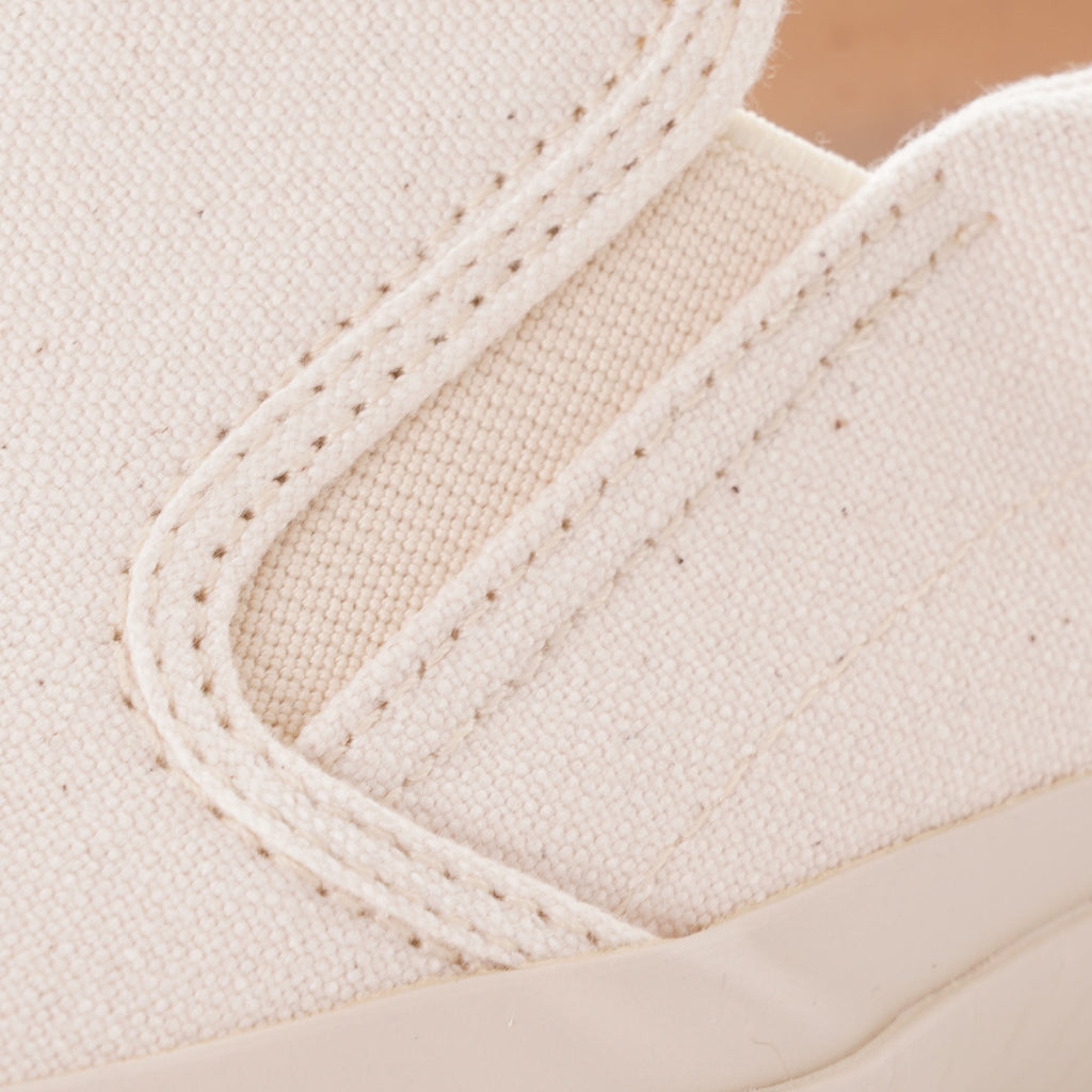 A close-up of the stitching and canvas material on the top of a white slip-on shoe.
