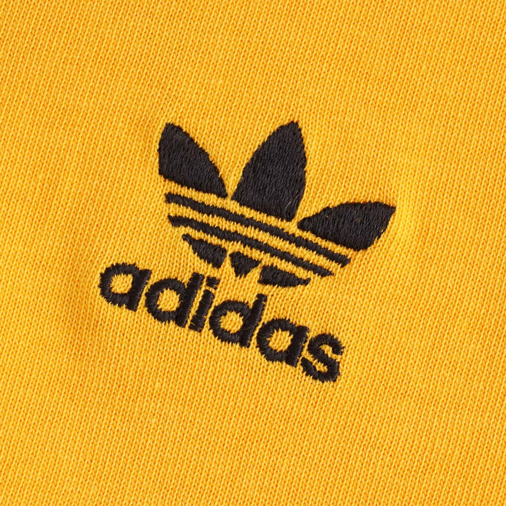 A close up of the black embroidered adidas trefoil logo on the orange t-shirt.