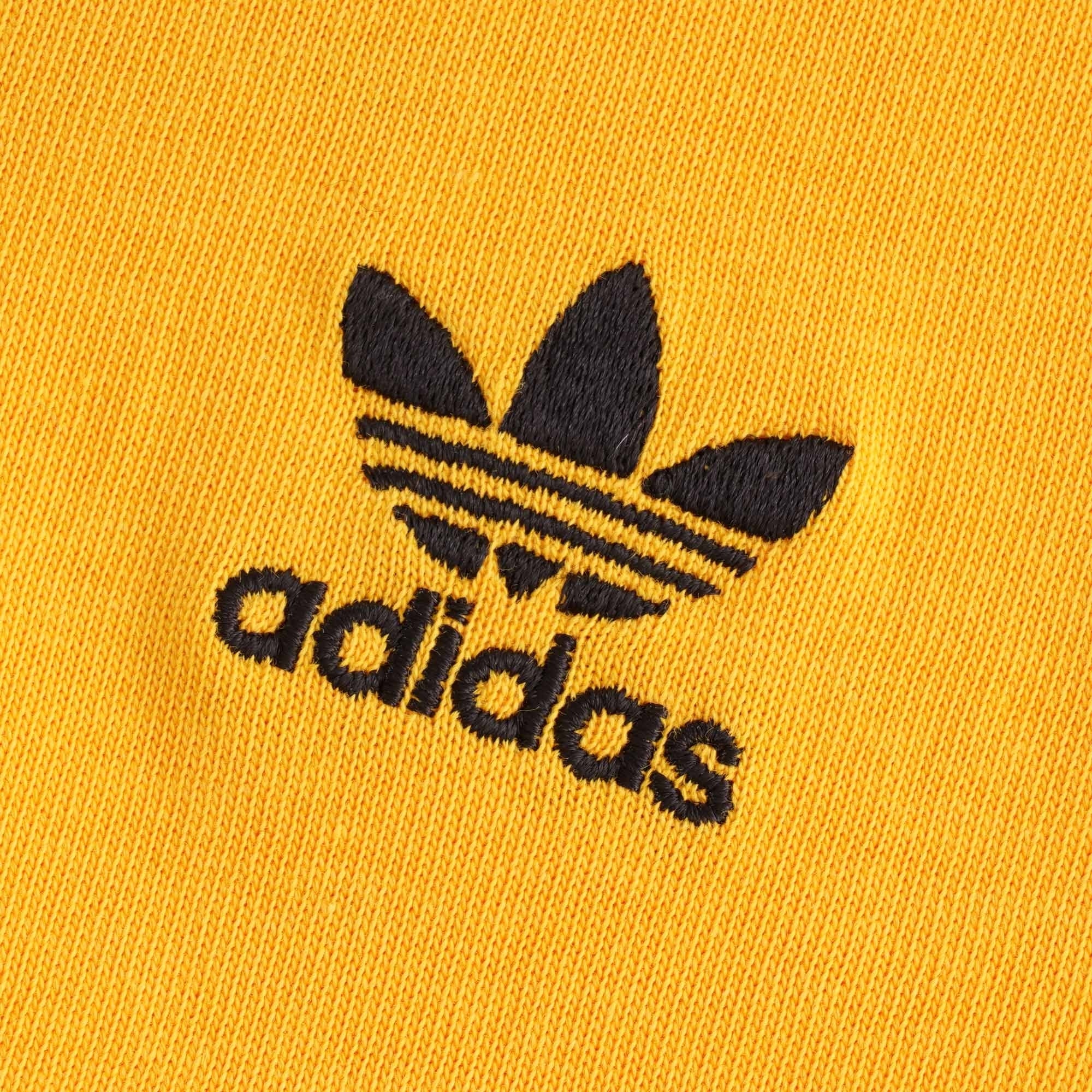 A close up of the black embroidered adidas trefoil logo on the orange t-shirt.