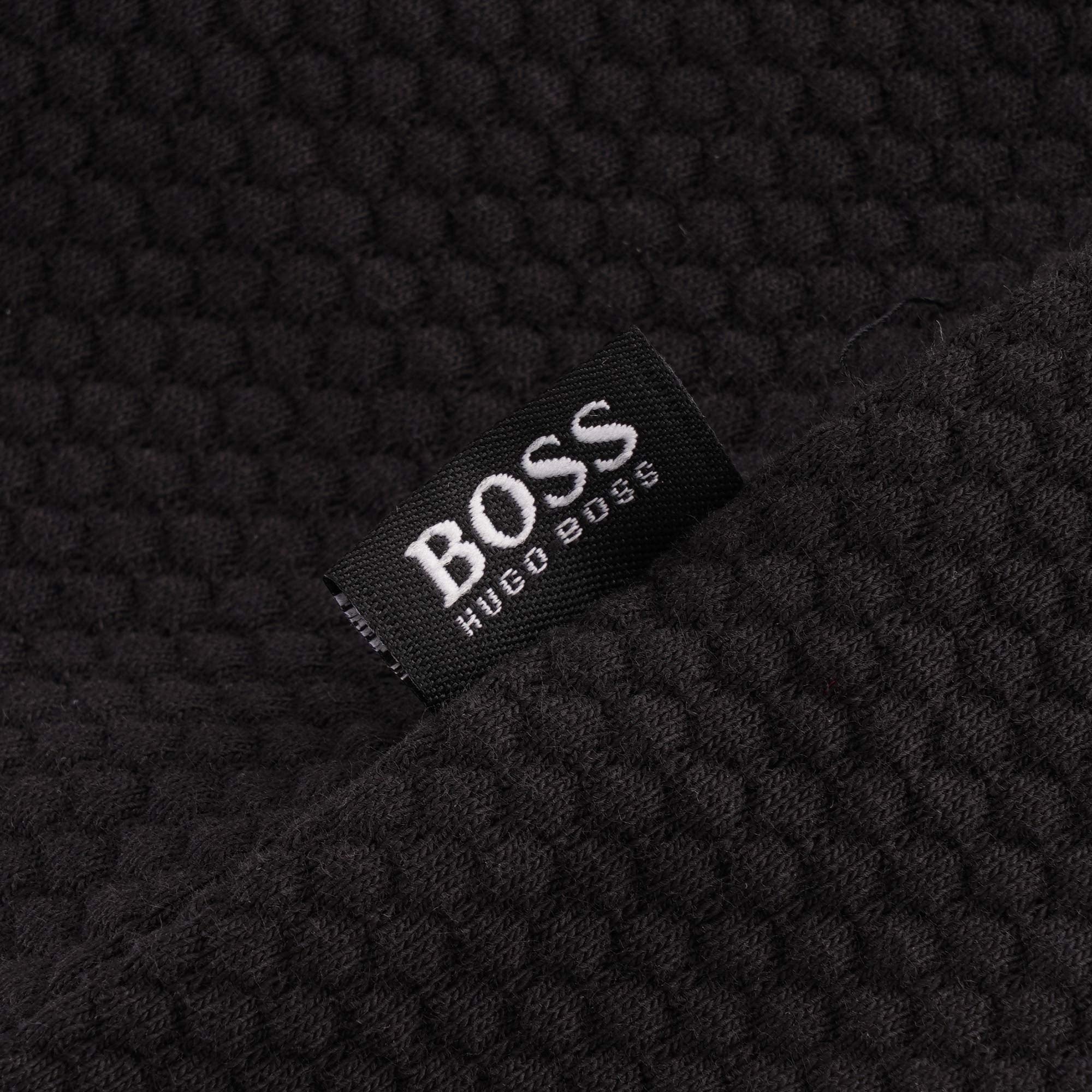 Close-up of the BOSS HUGO BOSS label on the black fabric of a polo shirt.