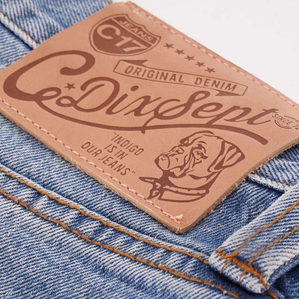 Close-up of a brown leather patch on blue jeans with 'CeDixSept' logo and a dog.