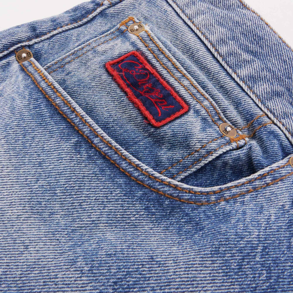 Close-up of the small front pocket of blue jeans with a red embroidered logo.