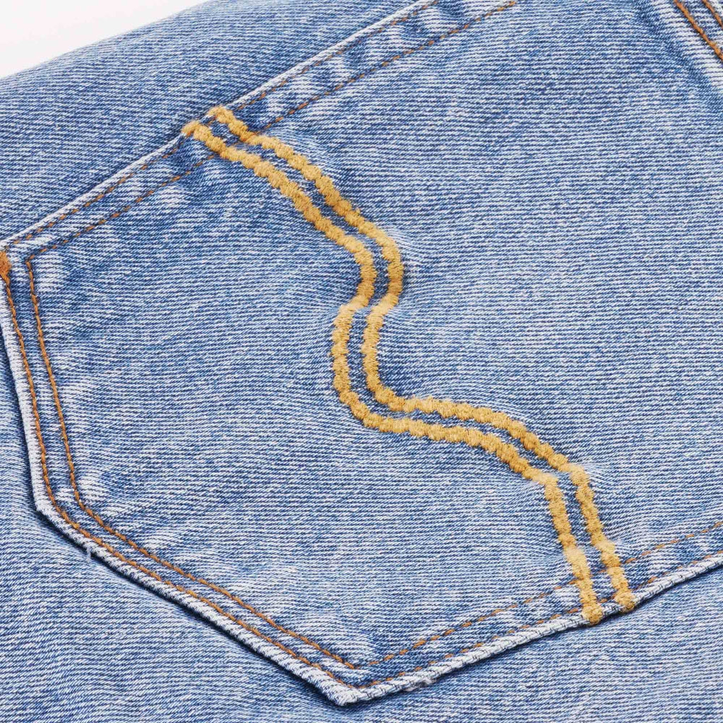Close-up of a back pocket of blue jeans with distinctive golden stitching.