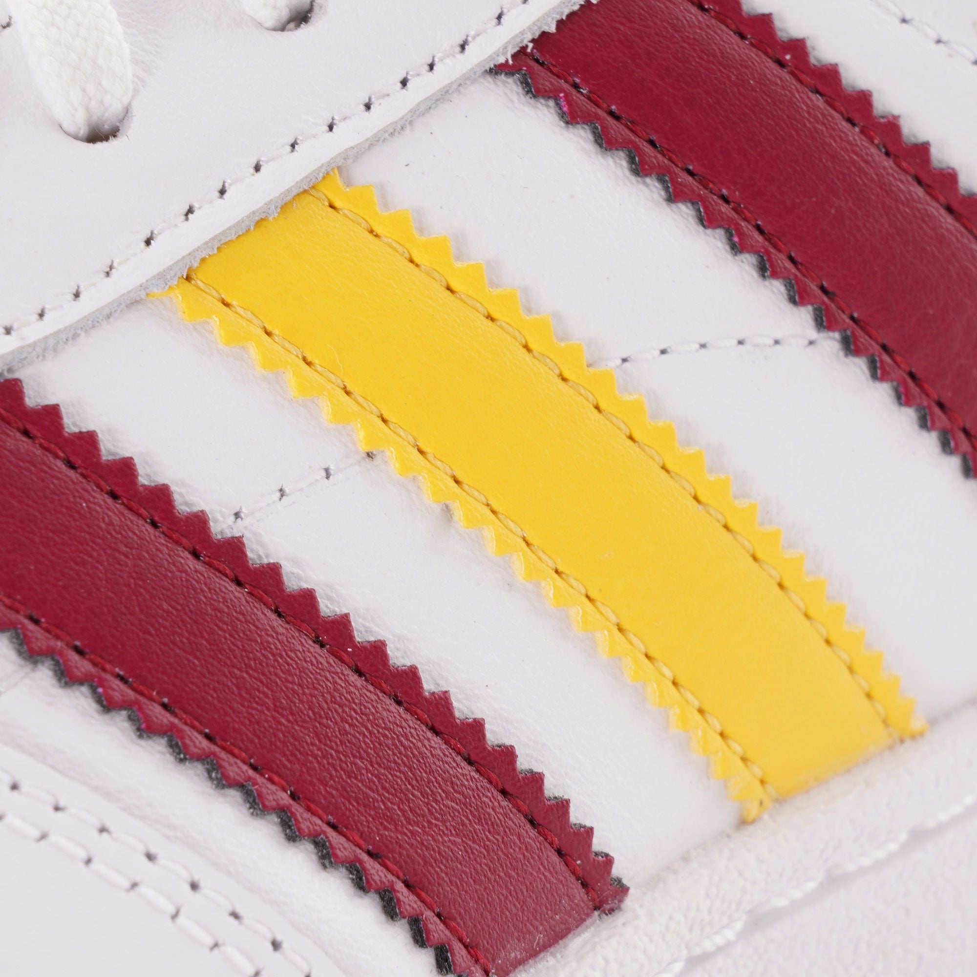 Close-up of the burgundy and yellow stripes on a white Adidas trainer.