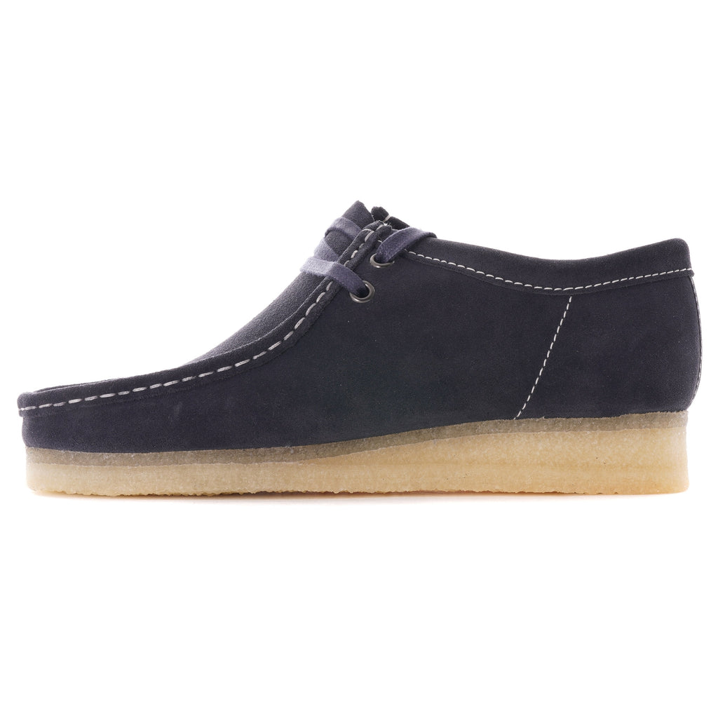 A single dark blue suede shoe with white stitching and a light brown crepe sole, side view.