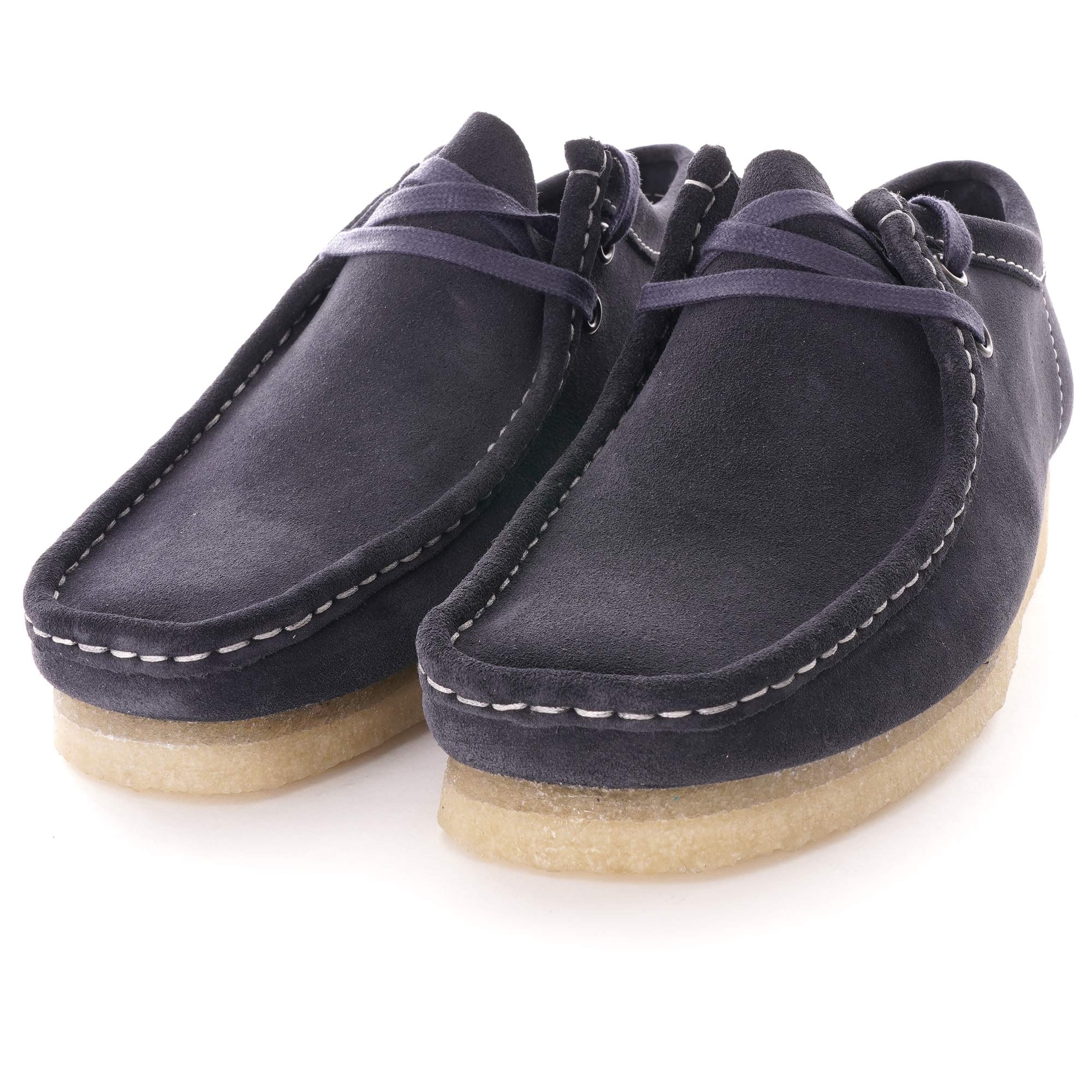A pair of dark blue suede shoes with white stitching and light brown crepe soles, angled view.