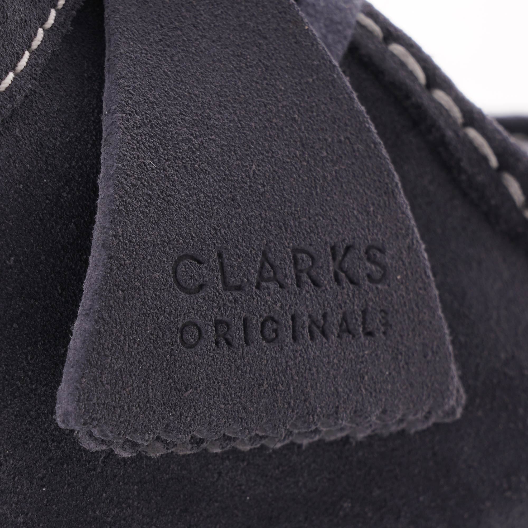 Close-up of the dark blue suede tag on the shoe with 'CLARKS ORIGINAL' embossed.