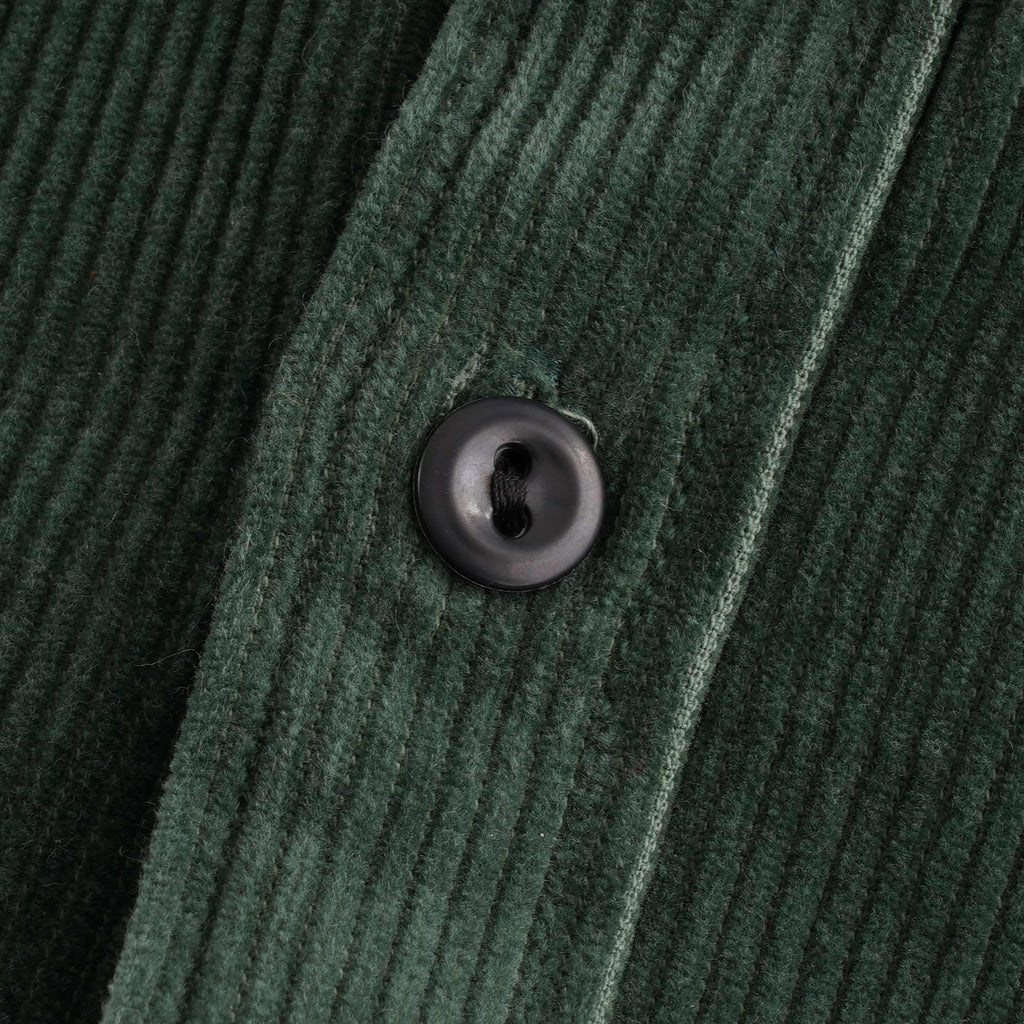Detailed close-up of a dark button on the green corduroy shirt.
