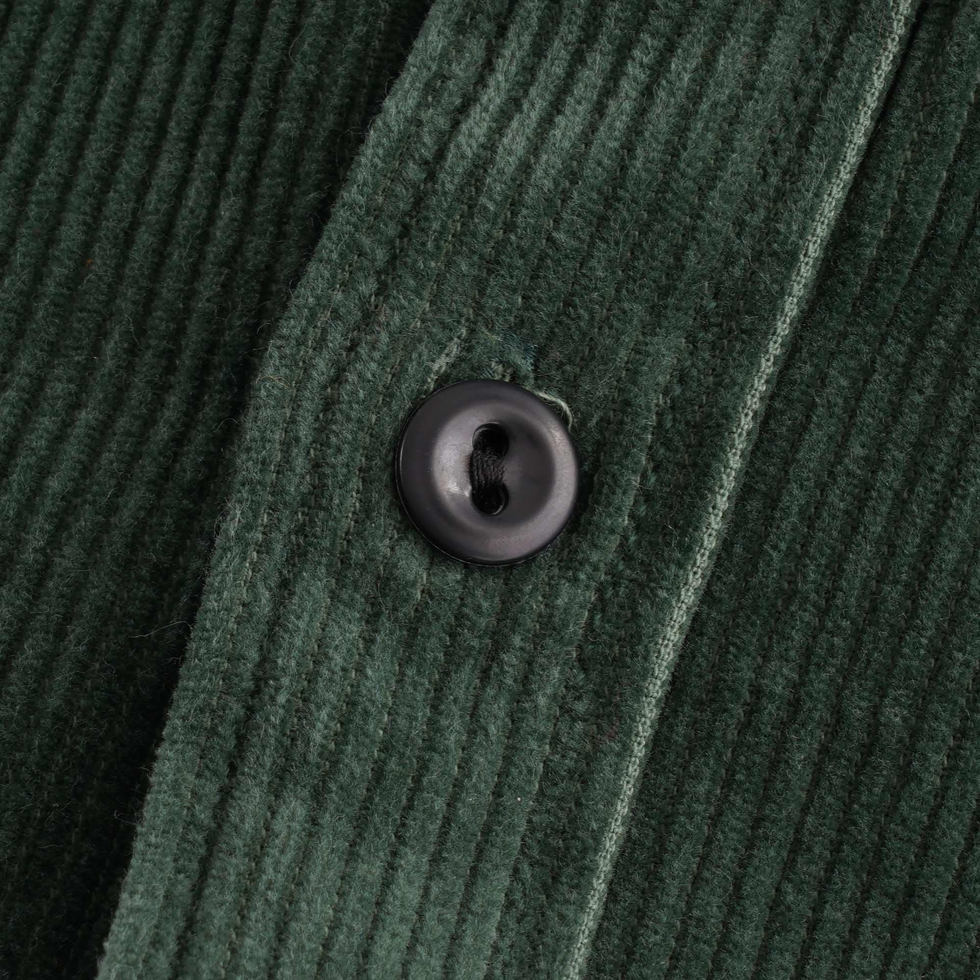 Detailed close-up of a dark button on the green corduroy shirt.