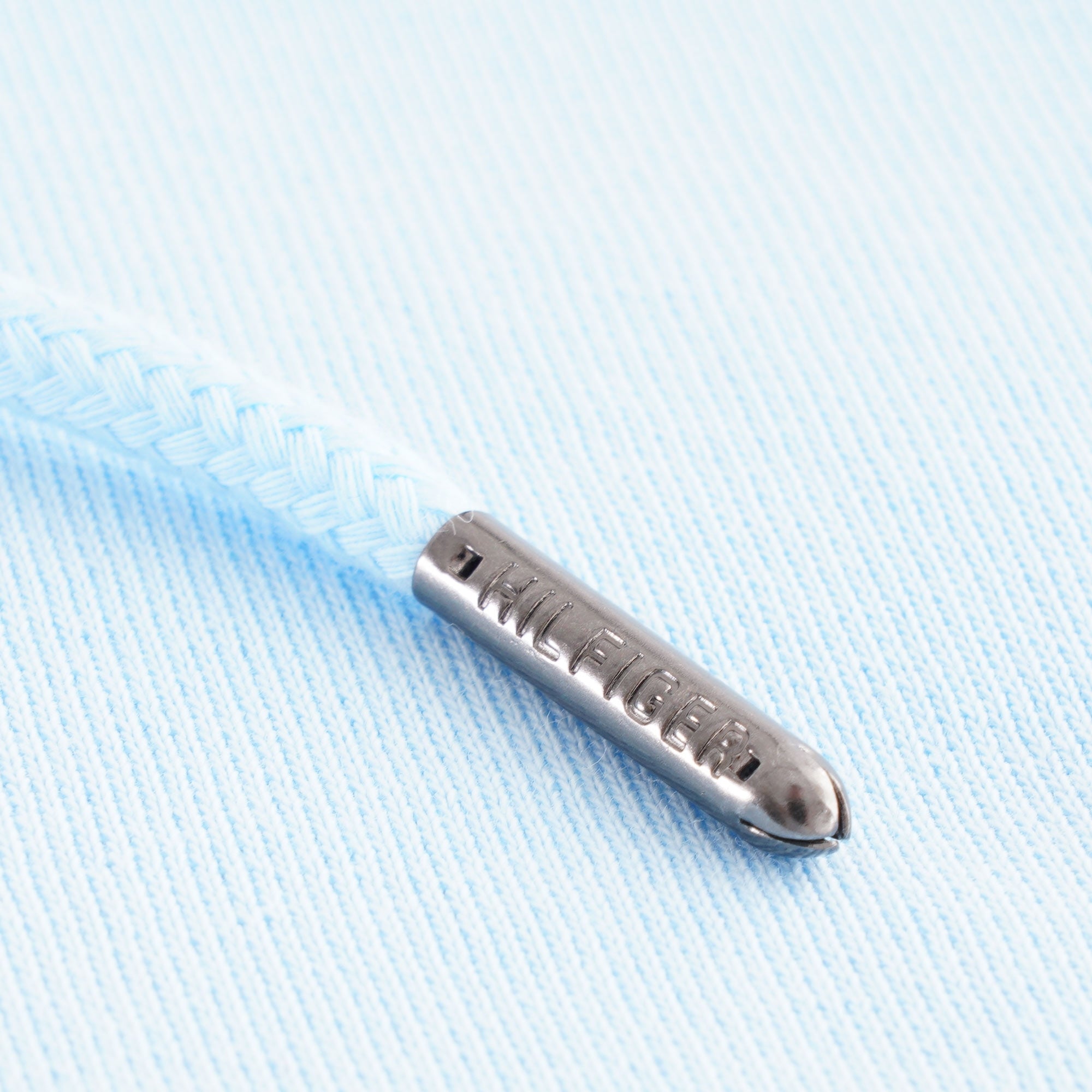 Close-up of the metal aglet on the light blue hoodie's drawstring.