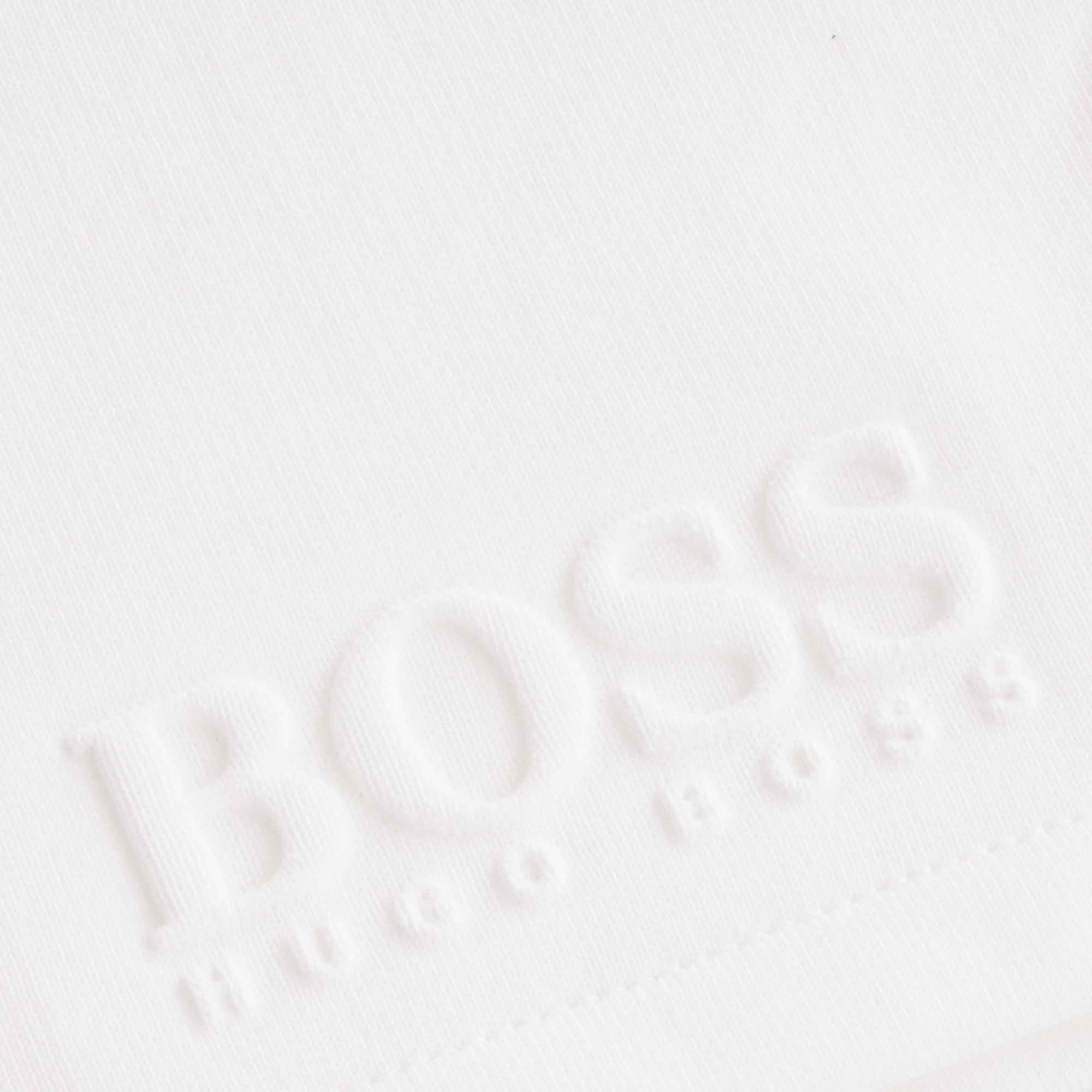 Close-up of embossed BOSS logo on white swim shorts.