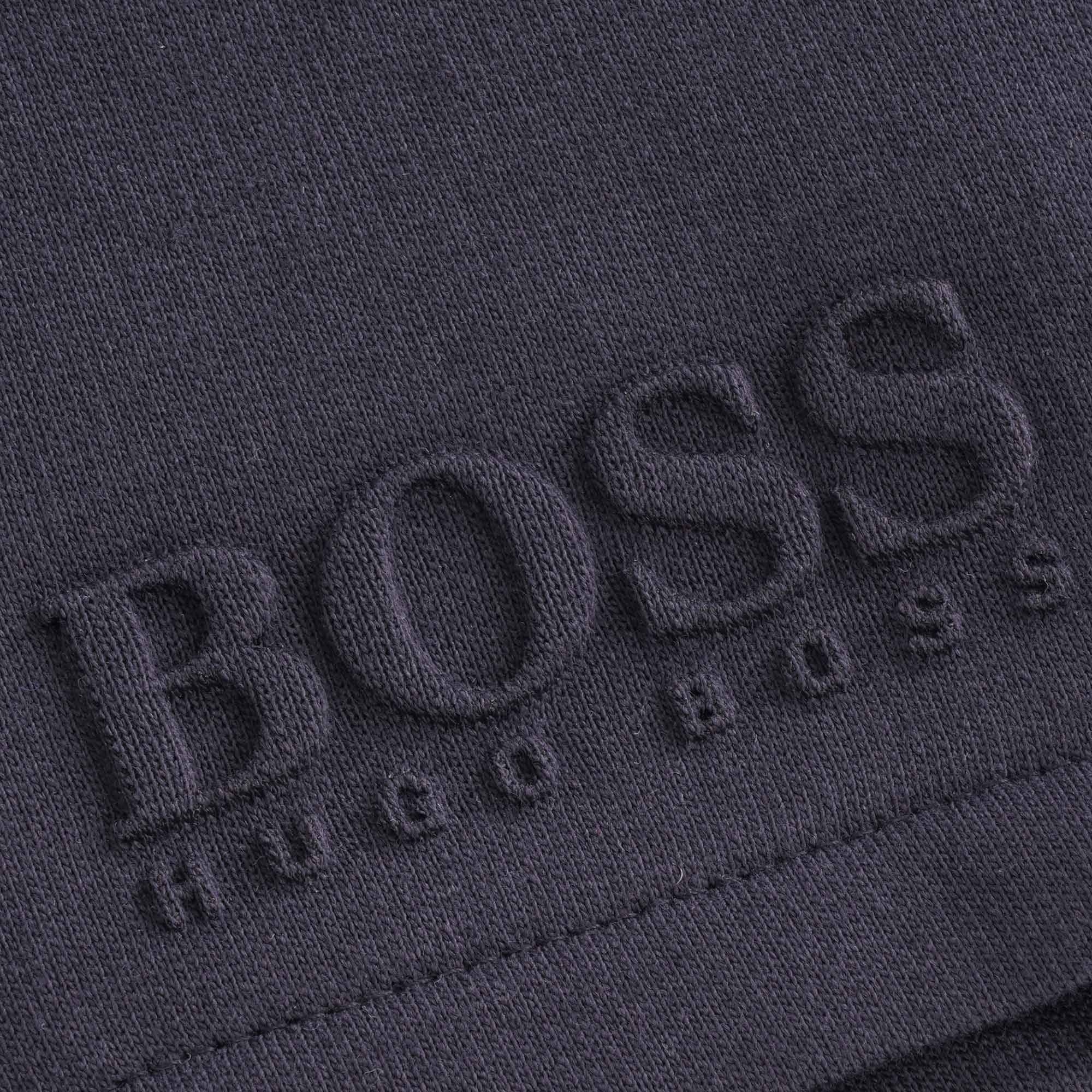 Close-up of the embossed BOSS Hugo Boss logo on the navy blue tracksuit shorts.