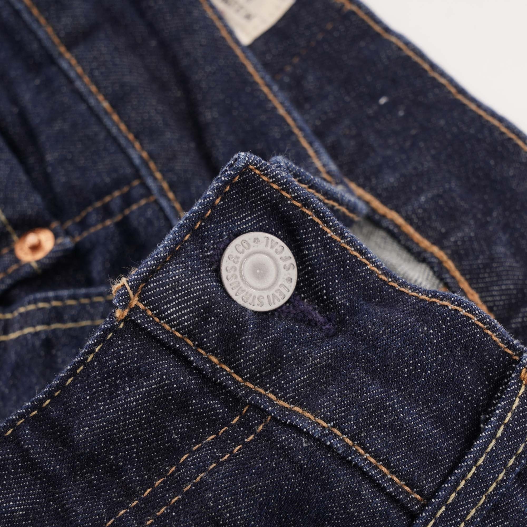 A close-up of the silver button and fly area of the dark wash Levi's jeans.