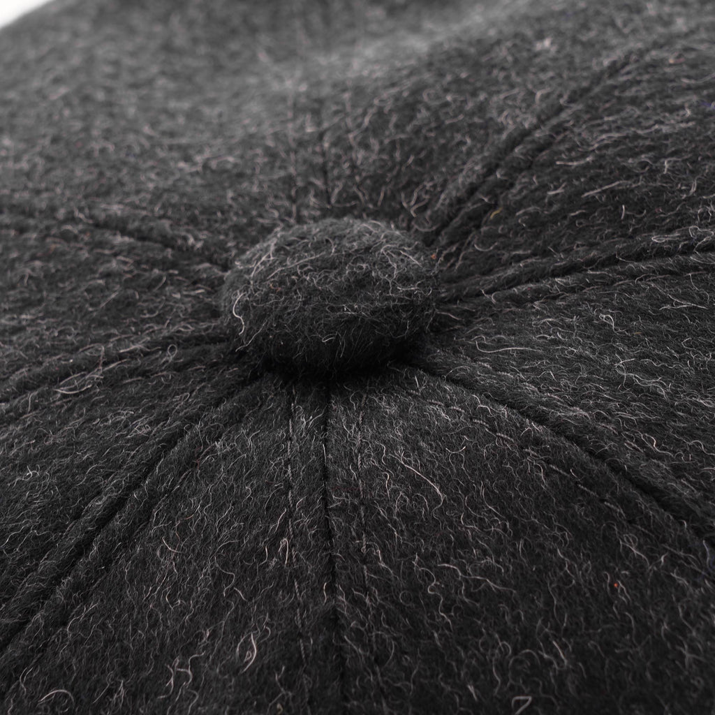 Close-up of the charcoal grey wool blend fabric and button detail on a flat cap.