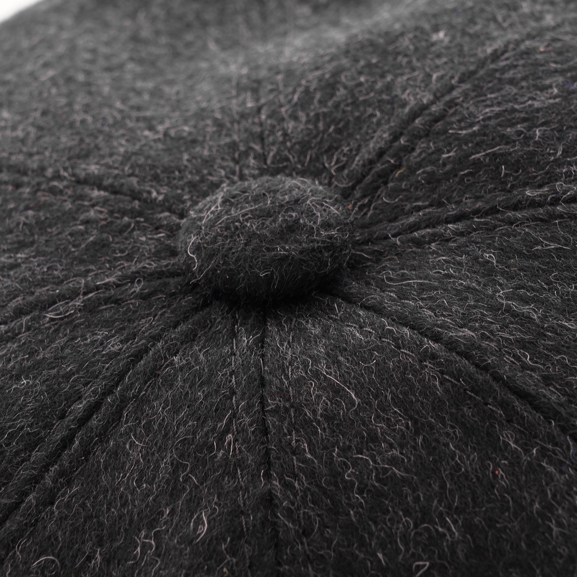 Close-up of the charcoal grey wool blend fabric and button detail on a flat cap.