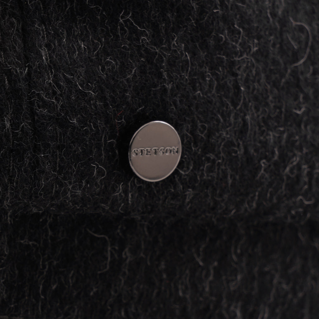 Close-up of a discreet metallic button with text on a charcoal grey wool blend flat cap.