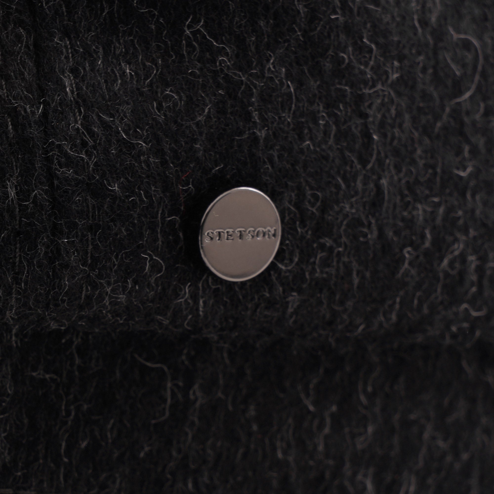 Close-up of a discreet metallic button with text on a charcoal grey wool blend flat cap.